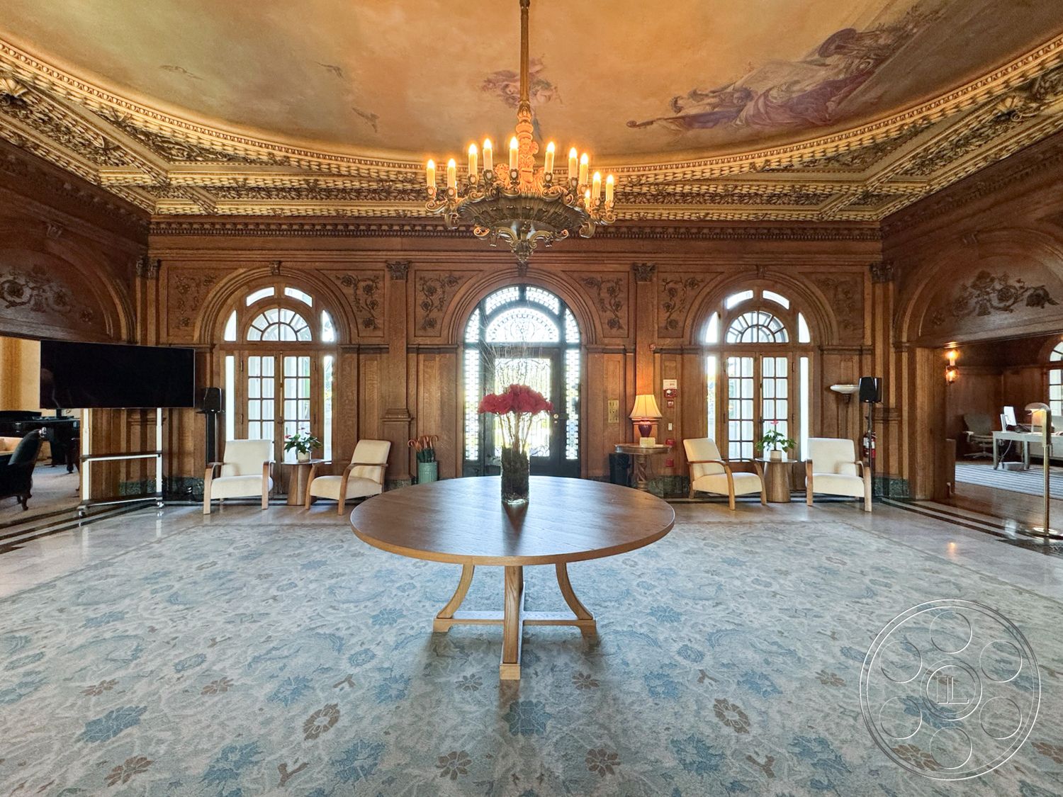 Adams Mansion - textured area rug, classic design elements, soft ambient lighting, large arched windows, elegant entryway, luxurious interior, traditional craftsmanship, elegant armchairs, round wooden dining table, ornate ceiling moldings, chandelier lighting fixture, historic architectural style, welcoming gathering space, natural light influx, interior decorative elements, rich wood paneling walls, intricate plaster ceiling details, marble flooring with floral pattern, fine art displays, grand entrance foyer