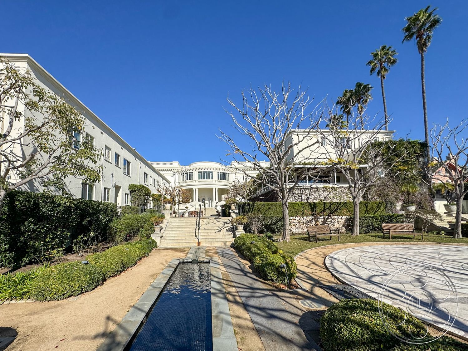 Adams Mansion - exterior, palm trees, concrete stairs, bench seating, stone pathway, modern architectural style, deck with railing, outdoor sitting area, manicured lawns, hedge landscaping, decorative stone walls, landscaped garden area, white painted walls, gravel garden path, stucco building facade, rectangular water feature, sunny urban environment, terraced planting beds, symmetrical building design, linear water channel