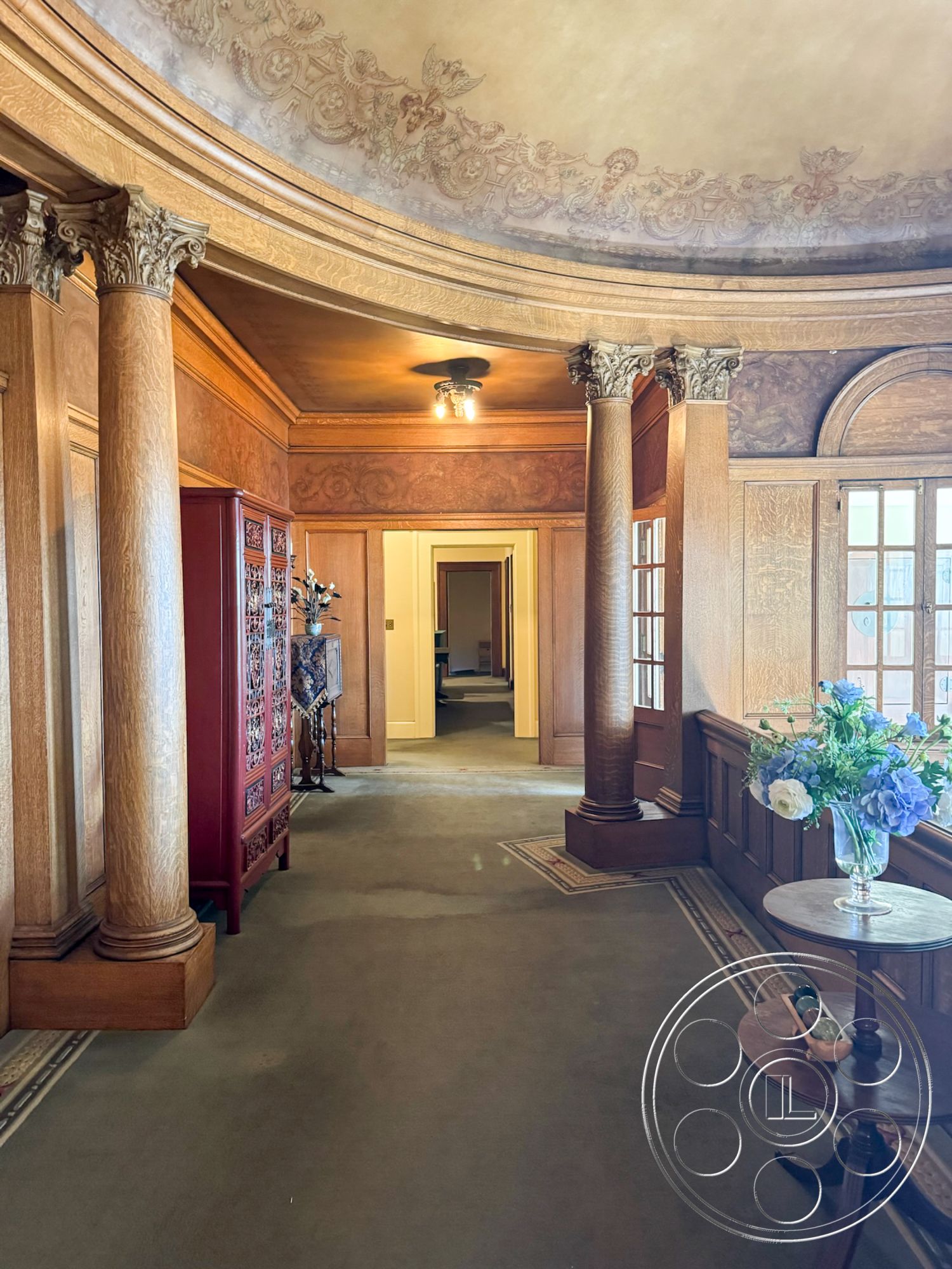 Adams Mansion - carpeted flooring, arched doorways, cohesive color palette, vintage wooden furniture, decorative column details, intricate plaster ceiling details, wood paneling hallway walls, ornate crown molding, elegant floral arrangement, traditional hallway lighting, classic architectural styles, exposed support columns, historic home features, ornate wall treatments