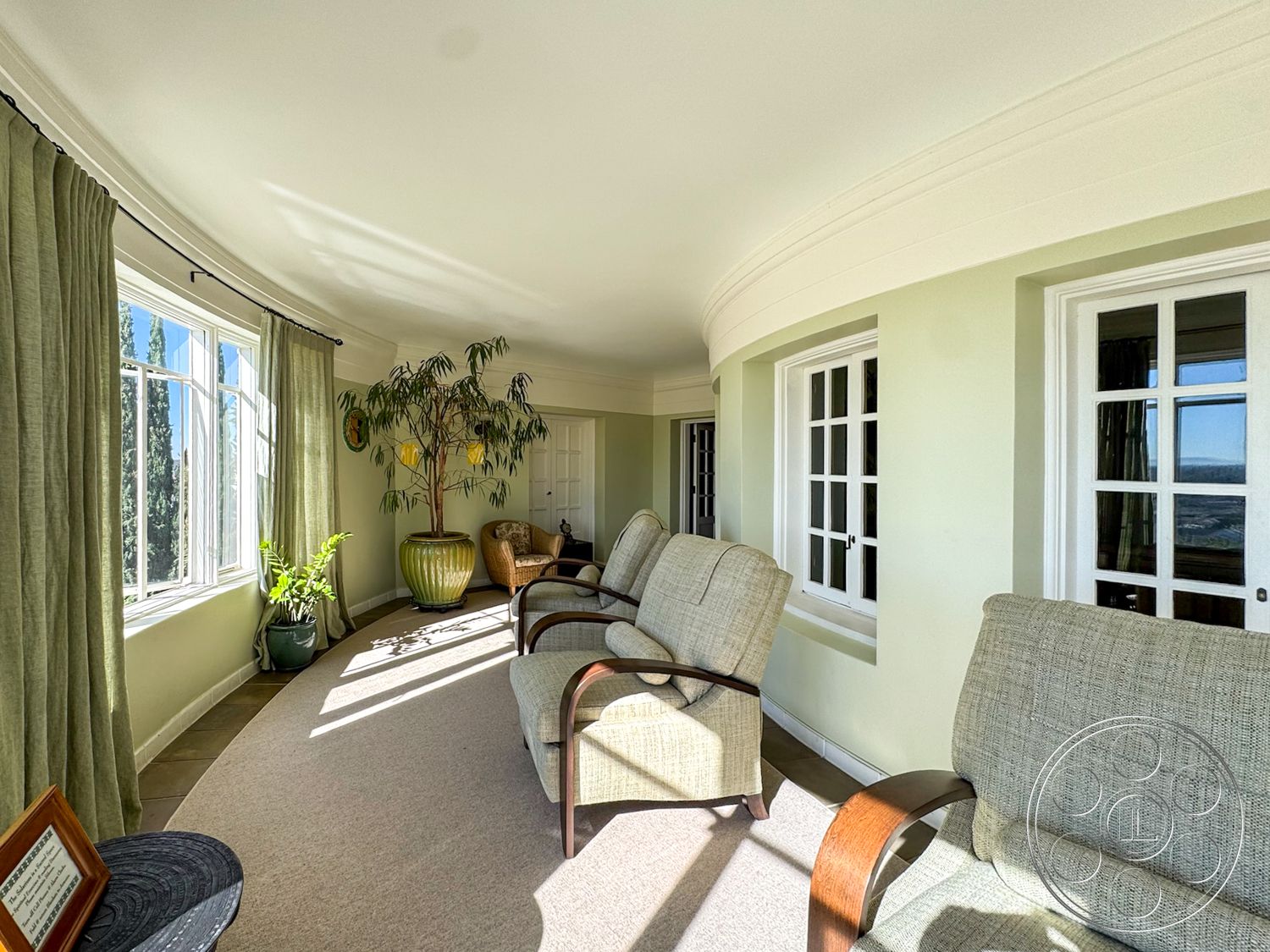 Adams Mansion - natural light, cozy seating area, carpet flooring, curved wall design, large windows with city view, interior sunroom, contemporary armchairs, light green painted walls, window with white wooden trim, potted indoor plant decor, soft curtain drapery, rounded ceiling details