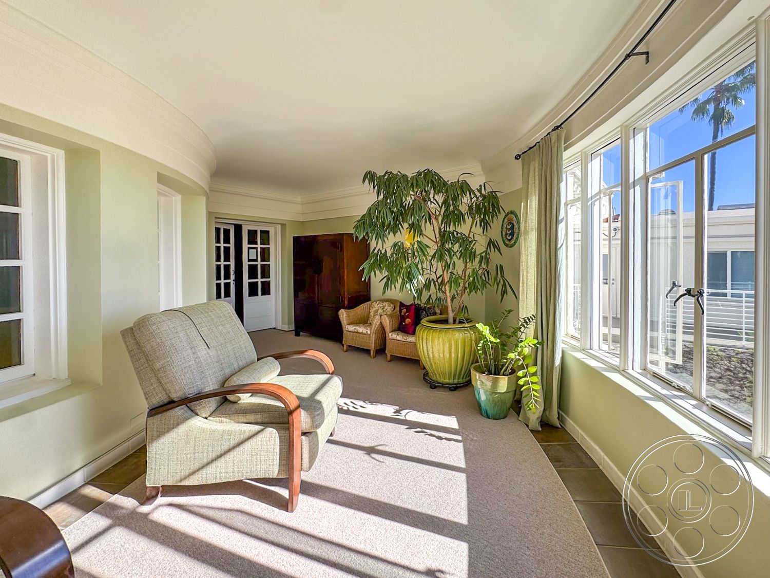 Adams Mansion - natural light, inviting atmosphere, potted plants, floor-to-ceiling windows, carpet flooring, circular seating arrangement, textured ceiling, mid-century modern furniture, cozy lounge area, white window frames, curved walls, suburban home setting, interior sunroom, large ceramic planter, green accent walls