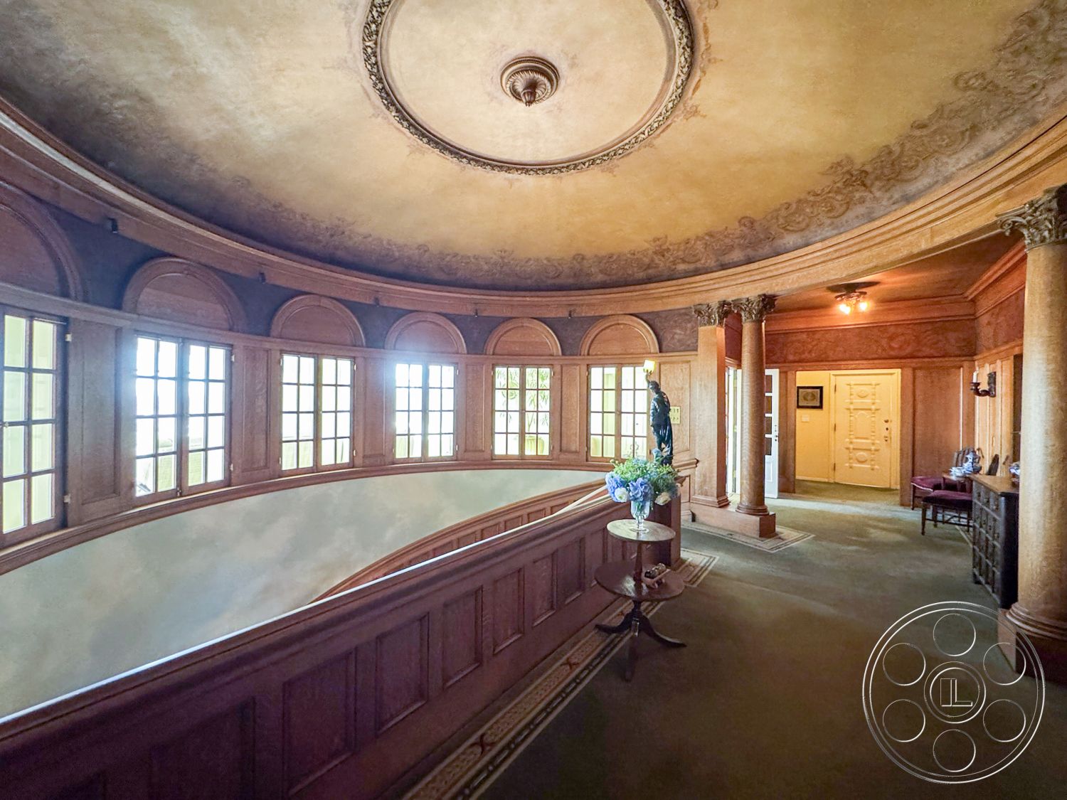 Adams Mansion - natural light from large windows, transom windows above doors, decorative wall moldings, exposed wood paneling interior, arched window shapes, double wooden doors, historic architectural style, curved balcony railings, coffered ceiling with intricate detailing, circular chandelier detail, intricate plaster ceiling ornamentation, marble floor inlay details, ornate decorative columns, glass panelled windows, carpet flooring in muted tones, elegant hallway design, spacious foyer area, artistic ceiling designs