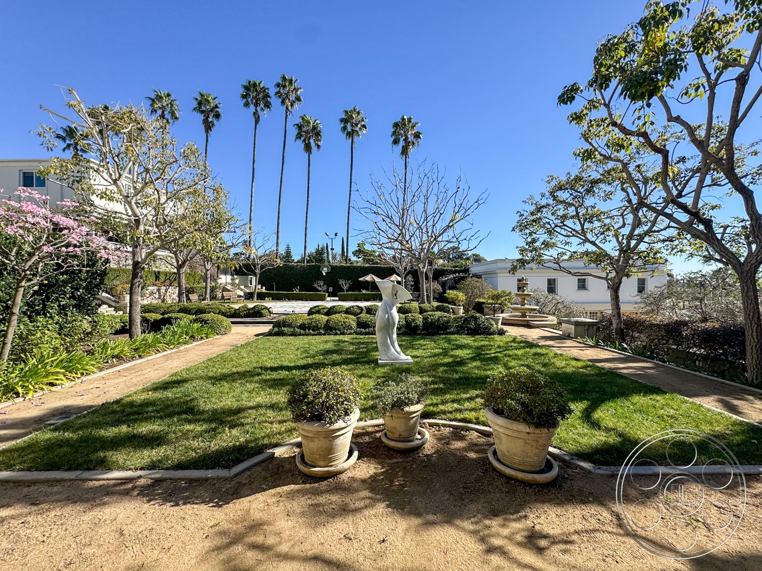 Adams Mansion - outdoor seating area, exterior landscaping, tall palm trees, manicured hedges, sunny outdoor environment, flowering plants in pots, suburban garden setting, terraced garden design, lawn area with ornamental shrubs, paved pathway with gravel border, stone planter pots, seasonal flowering trees, modern garden sculpture, fence line with shrubbery, drought-tolerant landscaping elements