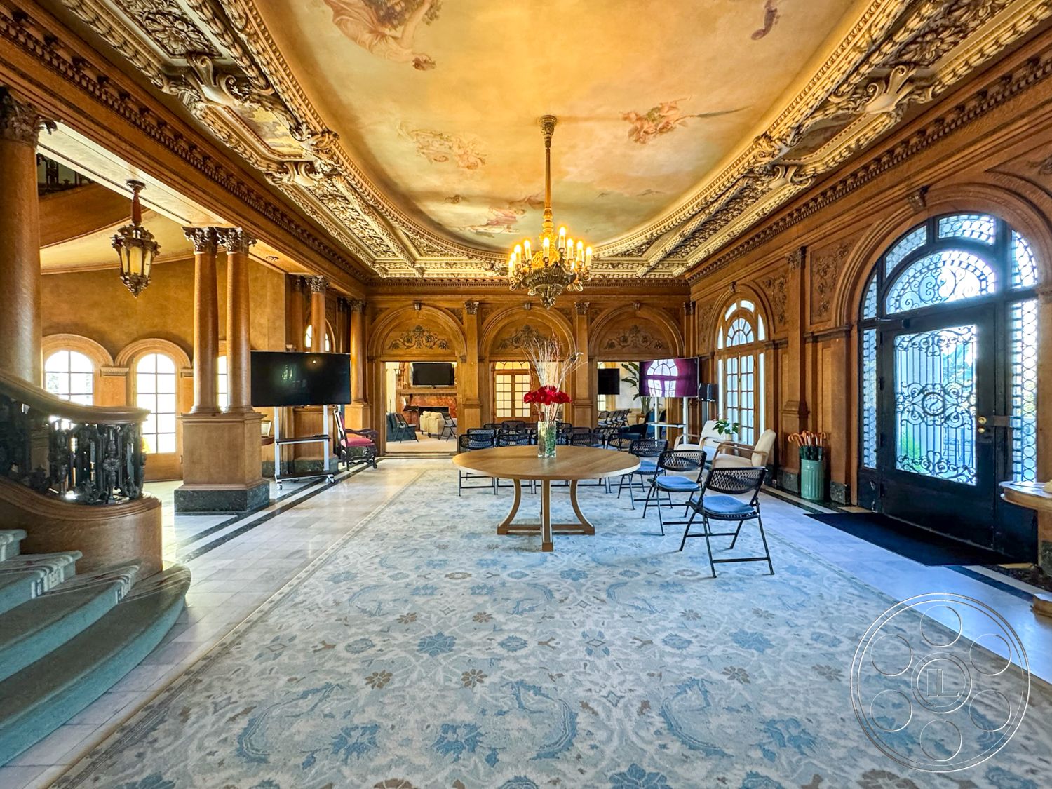 Adams Mansion - interior space, large arched windows, traditional area rug, marble foyer flooring, decorative chandelier lighting, exposed wooden railing, elegant round dining table, intricate plaster ceiling detailing, ornate wood paneling, gold leaf accents, arced wooden doorways, dark wood staircase, soft gold paint finish, stylish lounge seating, built-in entertainment area