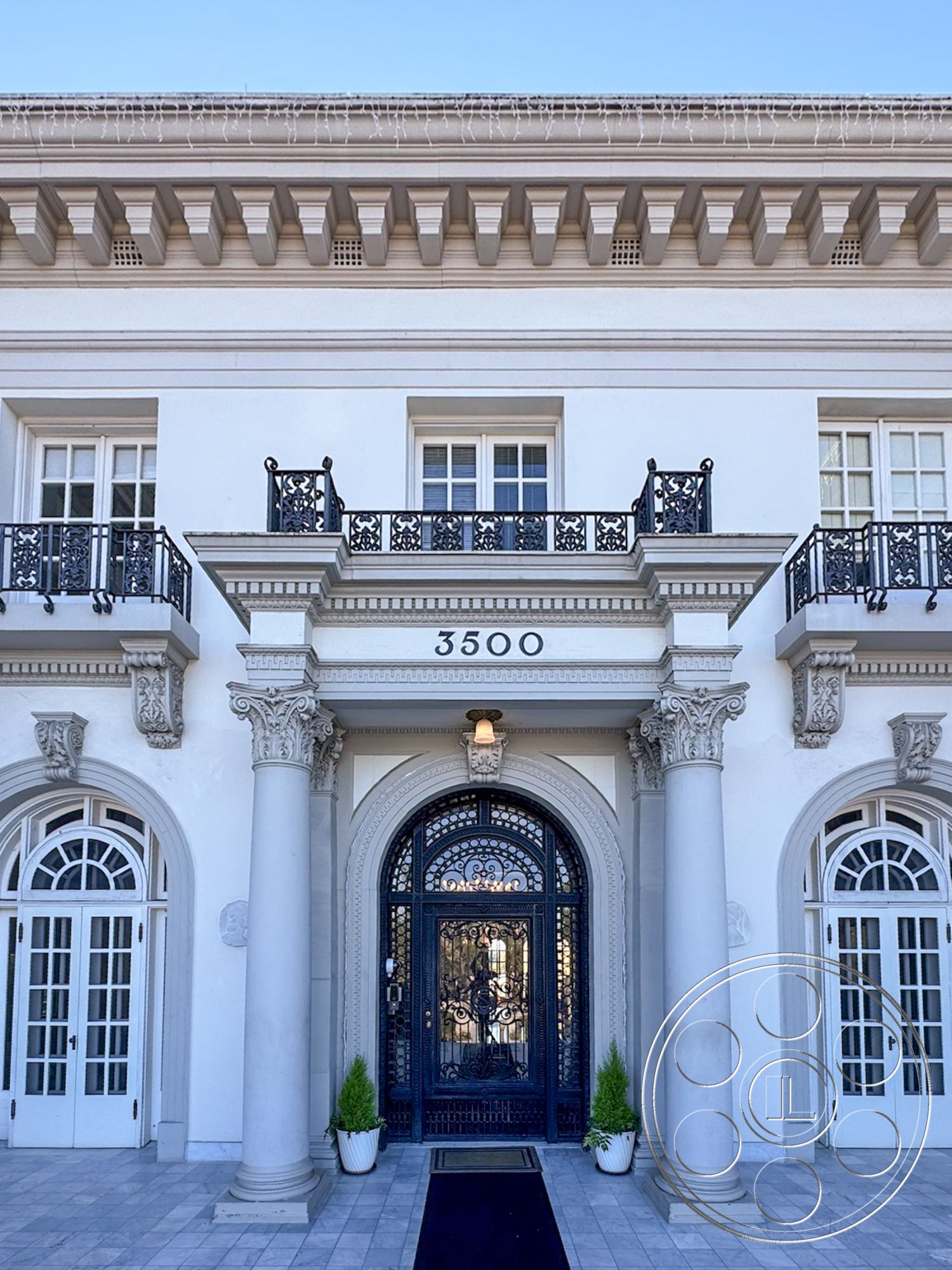 Adams Mansion - exterior, white stucco facade, columned entrance, landscaped front garden, textured stone entryway, decorative crown molding details, ornate wrought iron balcony railings, arched double doors, carved stone pilasters, geometric shaped window panes, symmetrical architectural elements, paver stone walkway, classical architectural style