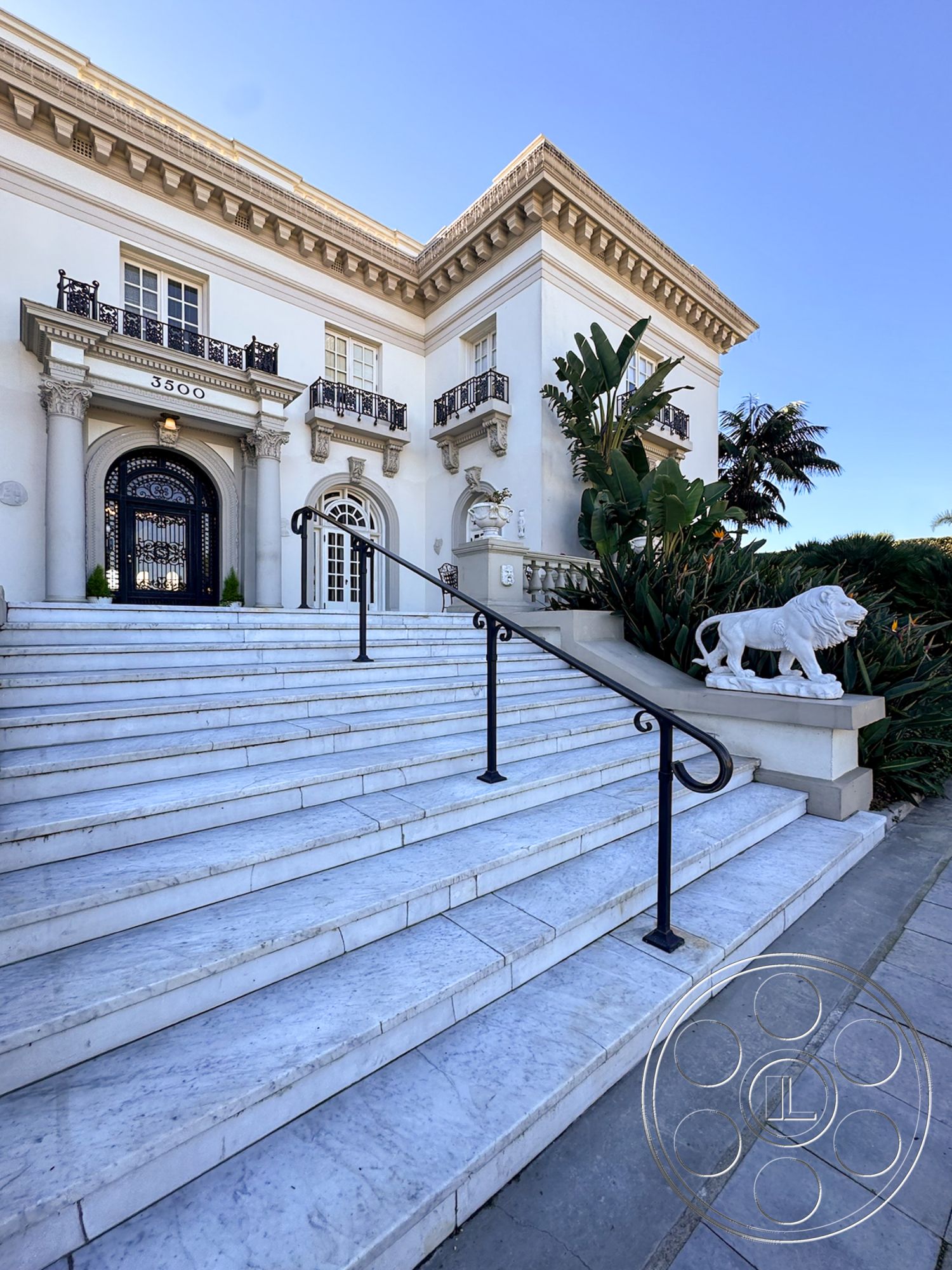 Adams Mansion - exterior, landscaped garden, lush tropical landscaping, black wrought iron railings, formal entryway, balcony with wrought iron railing, white painted walls, luxury residential property, classical architectural details, marble exterior steps, stone lion statue, grand entrance staircase, expansive urban view, ornate cornice details, neoclassical architectural style