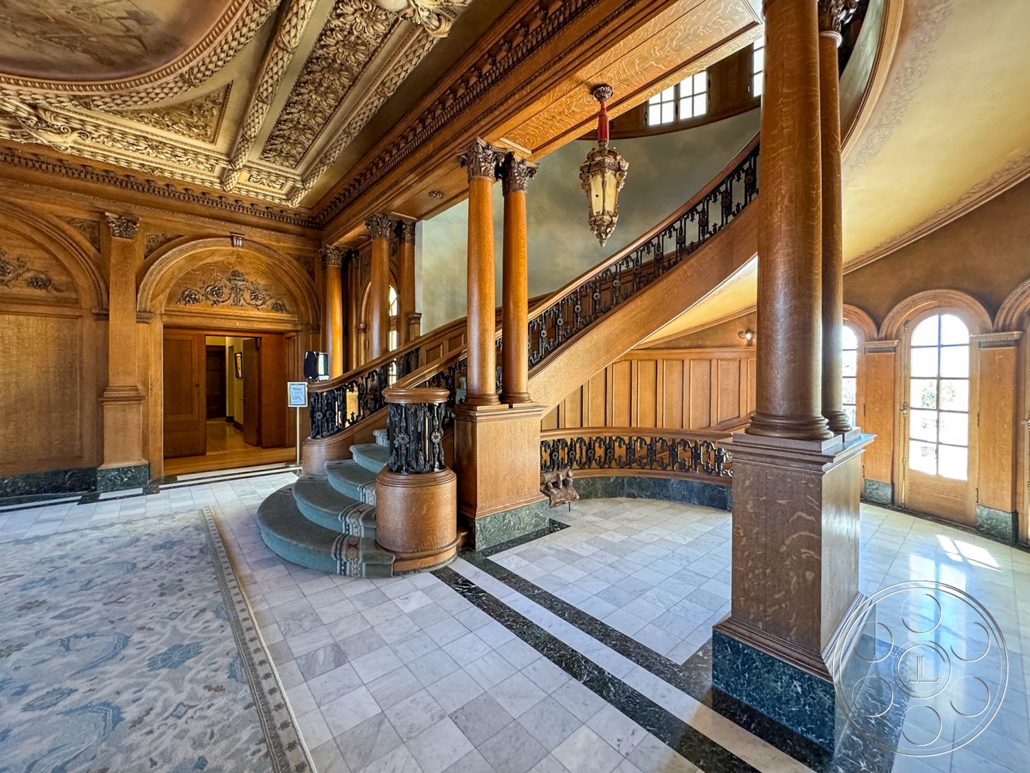 Adams Mansion - decorative crown molding, natural light from large windows, arched doorways, textured plaster walls, luxurious chandelier, exposed wood ceiling beams, marble foyer flooring, curved wooden railing, rich wood finishes, ornate wood paneling, interior grand staircase, intricate ceiling moldings, stone accent pillars, black and white checkered entryway, classic Victorian architectural style, elegant landing space, spacious open foyer, artistic wall carvings, multi-layered ceiling design