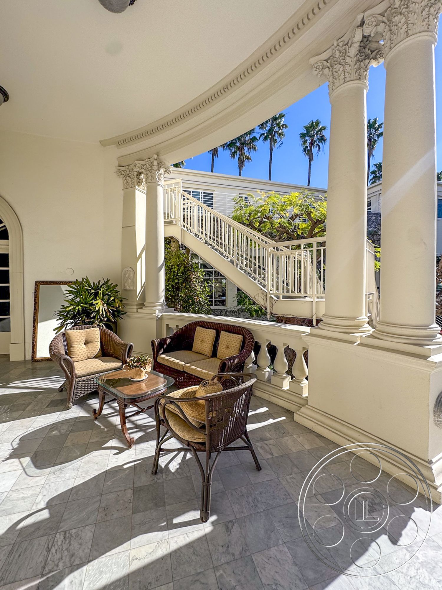 Adams Mansion - natural light, spiral staircase, tropical landscaping, textured plaster walls, exterior seating area, palm tree view, southern California architecture, sunny outdoor setting, urban residential environment, marble patio flooring, glass-top coffee table, curved colonnade, wicker patio furniture, ornate column details