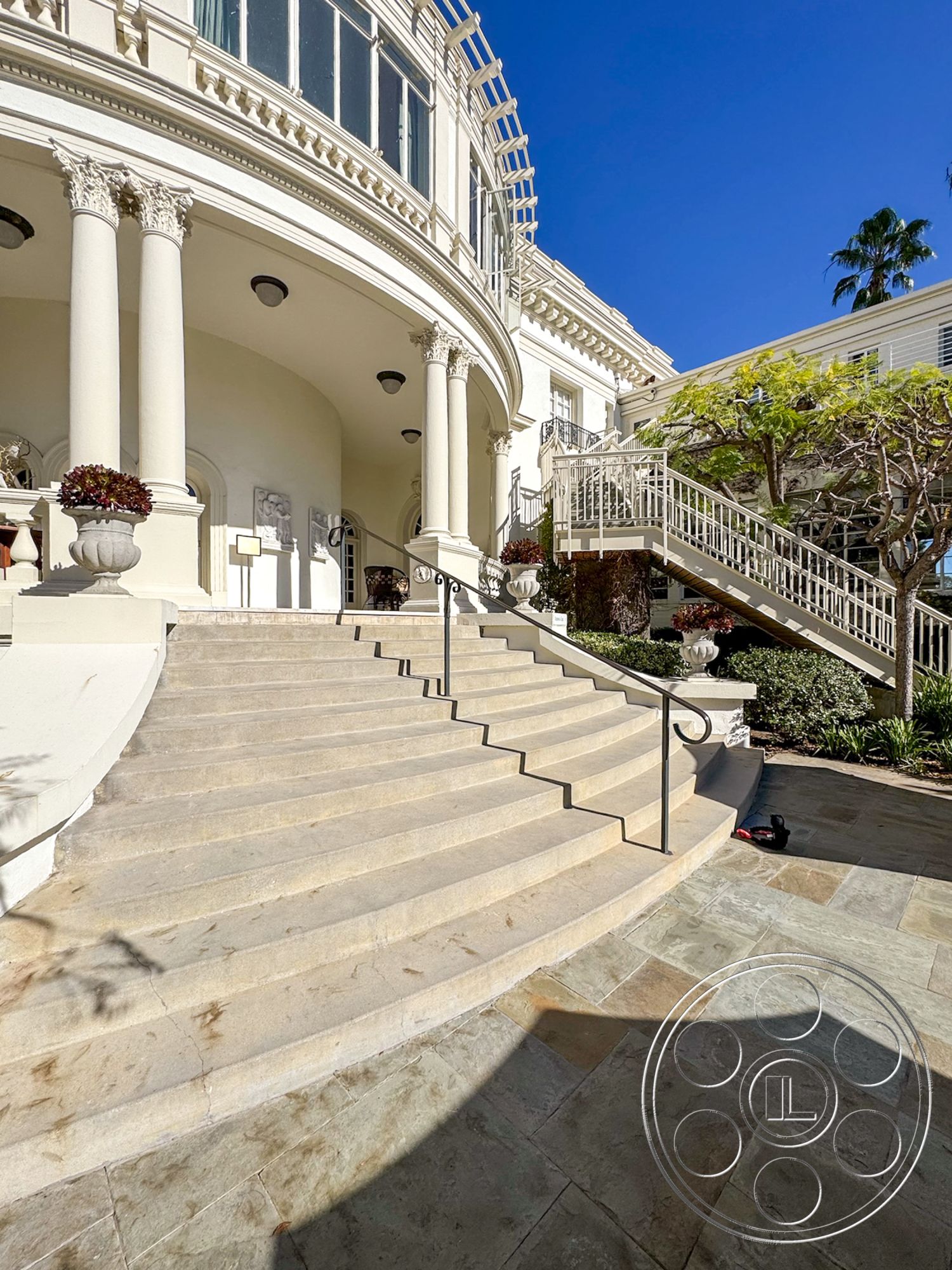 Adams Mansion - exterior, landscaped garden, white stucco walls, outdoor seating area, surrounding greenery, floor-to-ceiling windows, symmetrical facade, arched entryway, classic architectural details, poolside view, balustrade railings, ornate column design, limestone staircase steps, curved stone patio flooring, palatial entrance, modern terrace design