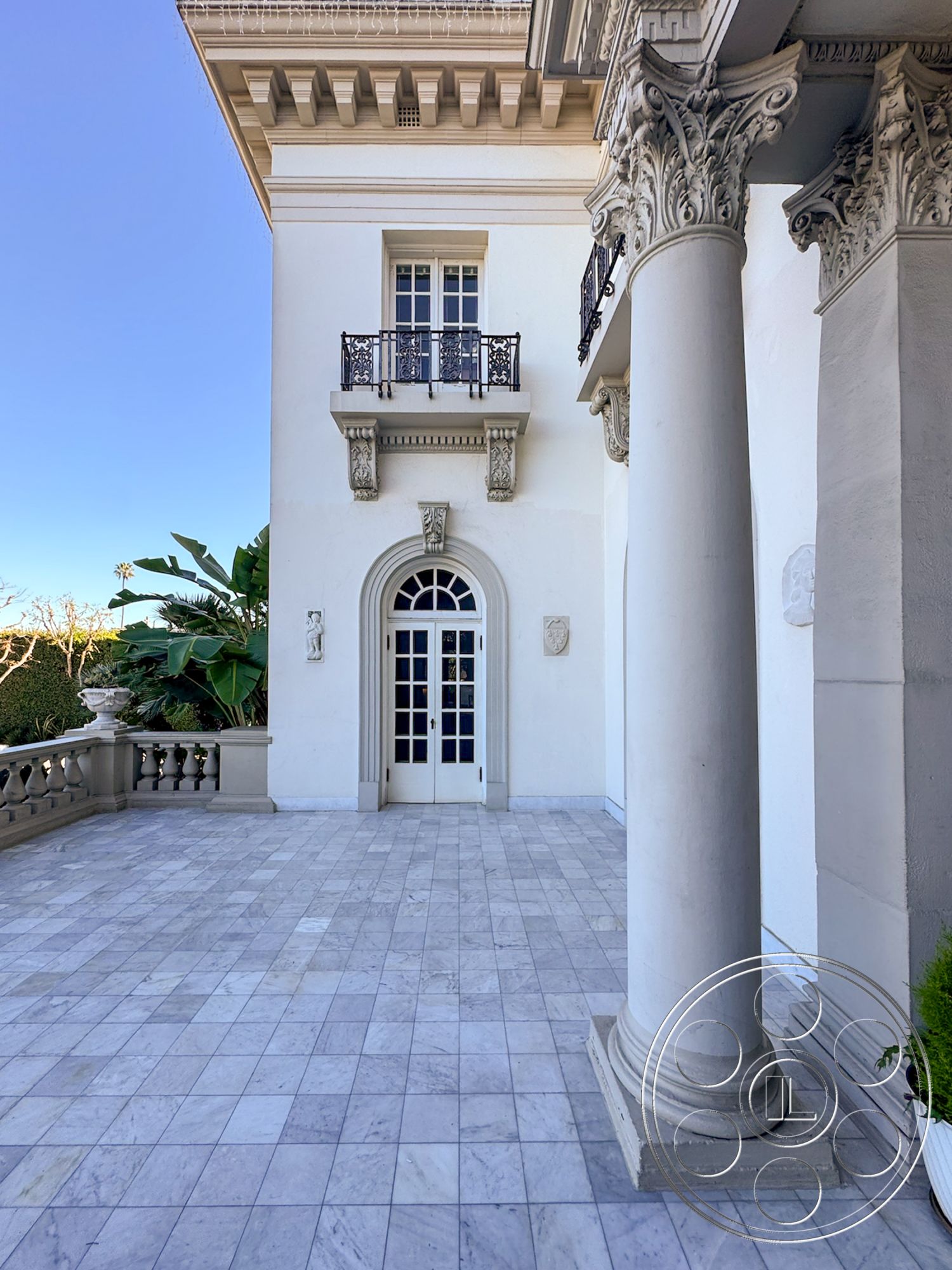 Adams Mansion - exterior white stucco walls, exterior landscaped garden setting, exterior recessed lighting fixtures, exterior marble patio flooring, exterior decorative column with Corinthian capital, exterior wrought iron balcony railing, exterior double door entrance with traditional paneling, exterior archway entry, exterior stone balustrade, architectural details of traditional design, exterior geometric column bases, exterior symmetrical facade design, exterior ornate frieze details, exterior classical architectural style