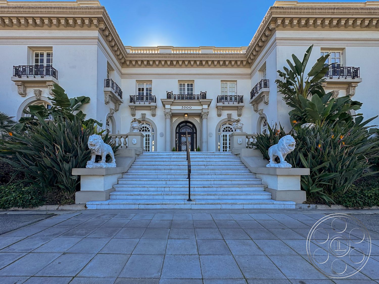 Adams Mansion - exterior, white stucco walls, landscaped gardens, floor-to-ceiling windows, symmetrical facade, arched doorways, paved stone walkway, marble front steps, grand entrance staircase, ornate balustrades, stone lion statues, decorative cornice detailing, modern tropical landscaping, gabled roof elements, double doors entrance, modern classical architecture, expansive courtyard area, luxury mansion entrance