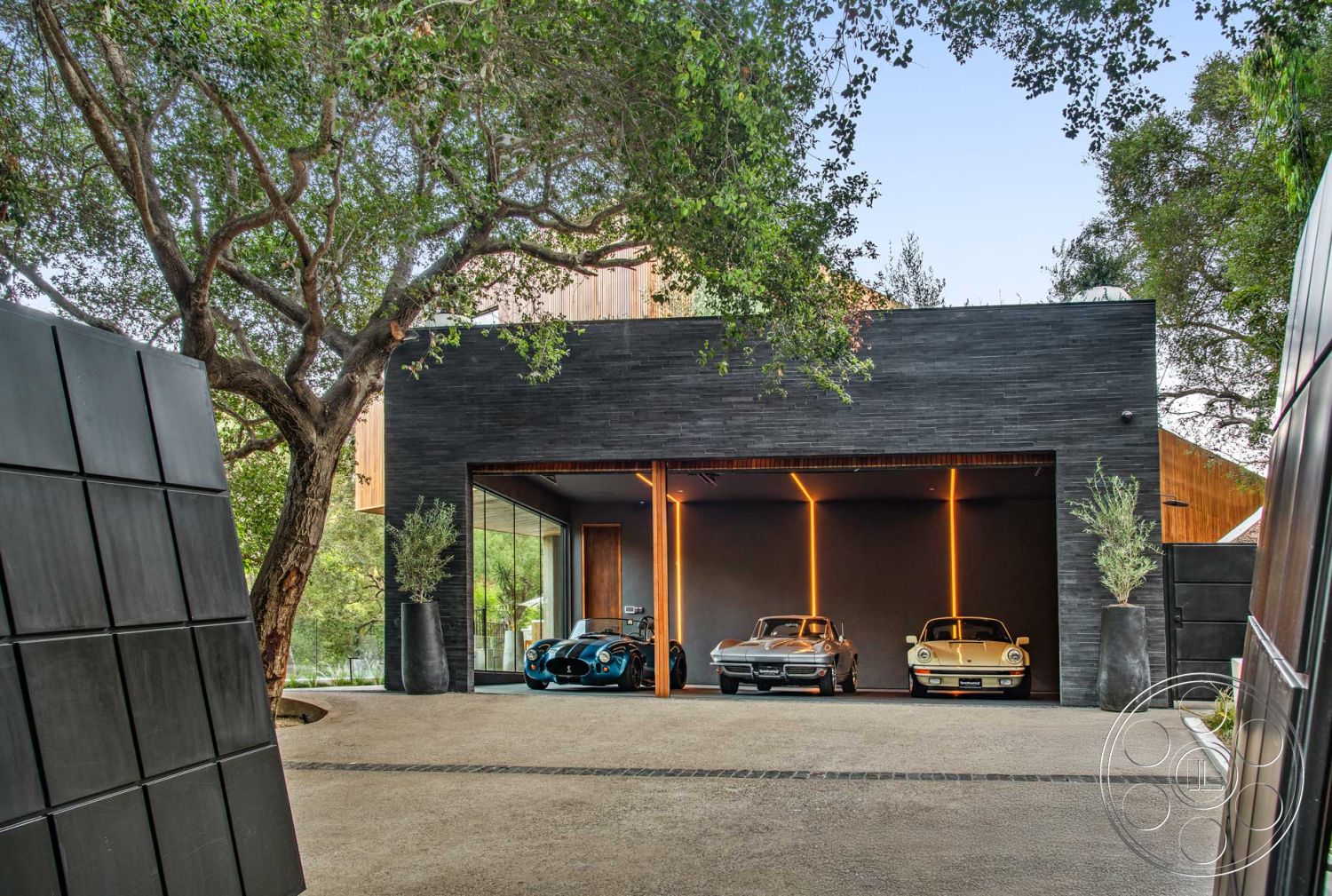 Modern 520 - exterior, smooth concrete surface, modern architectural style, minimalist landscaping, large oak trees, vertical wooden slats, integrated lighting fixtures, natural landscape setting, contemporary home design, rectangular driveway, floor-to-ceiling glass doors, open garage layout, slate stone facade, textured black stone walls, wood paneling accent, gravel driveway surface, outdoor planter features, luxury car display area