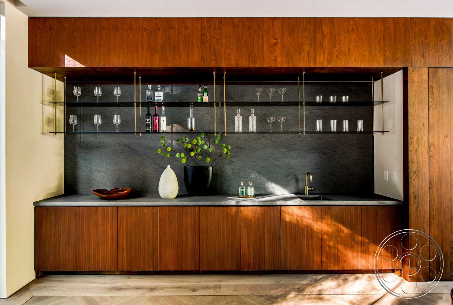 Modern 520 - neutral color palette, contemporary style, decorative vase, minimalist design elements, marble bar top, textured wall treatment, sleek faucet design, greenery decor, black stone countertop, interior bar area, wood cabinetry with a warm finish, glass wall shelves, gold accents in shelving supports, textured stone wall backing, modern glassware display, natural lighting elements, herringbone patterned floor