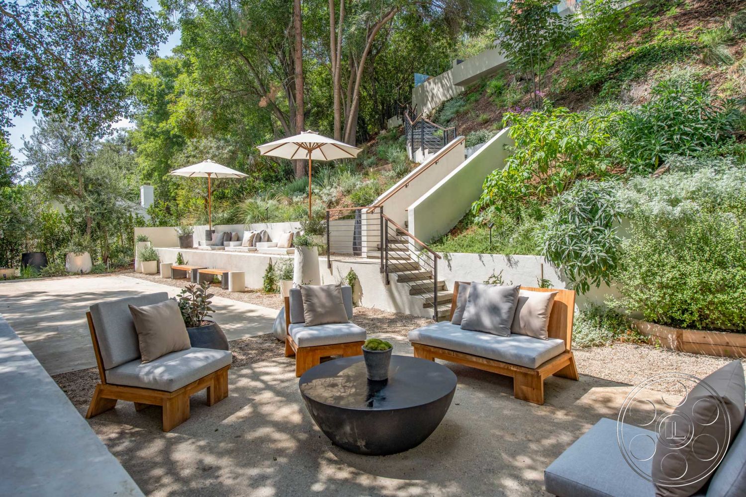 Modern 520 - gravel pathway, metal railing staircase, residential landscaping, minimalist outdoor space, exterior concrete patio floor, lush greenery surrounding, sunny backyard setting, urban hillside environment, wooden lounge seating, concrete seating wall, round black stone coffee table, modern patio umbrellas, tiered garden design, concrete steps leading up