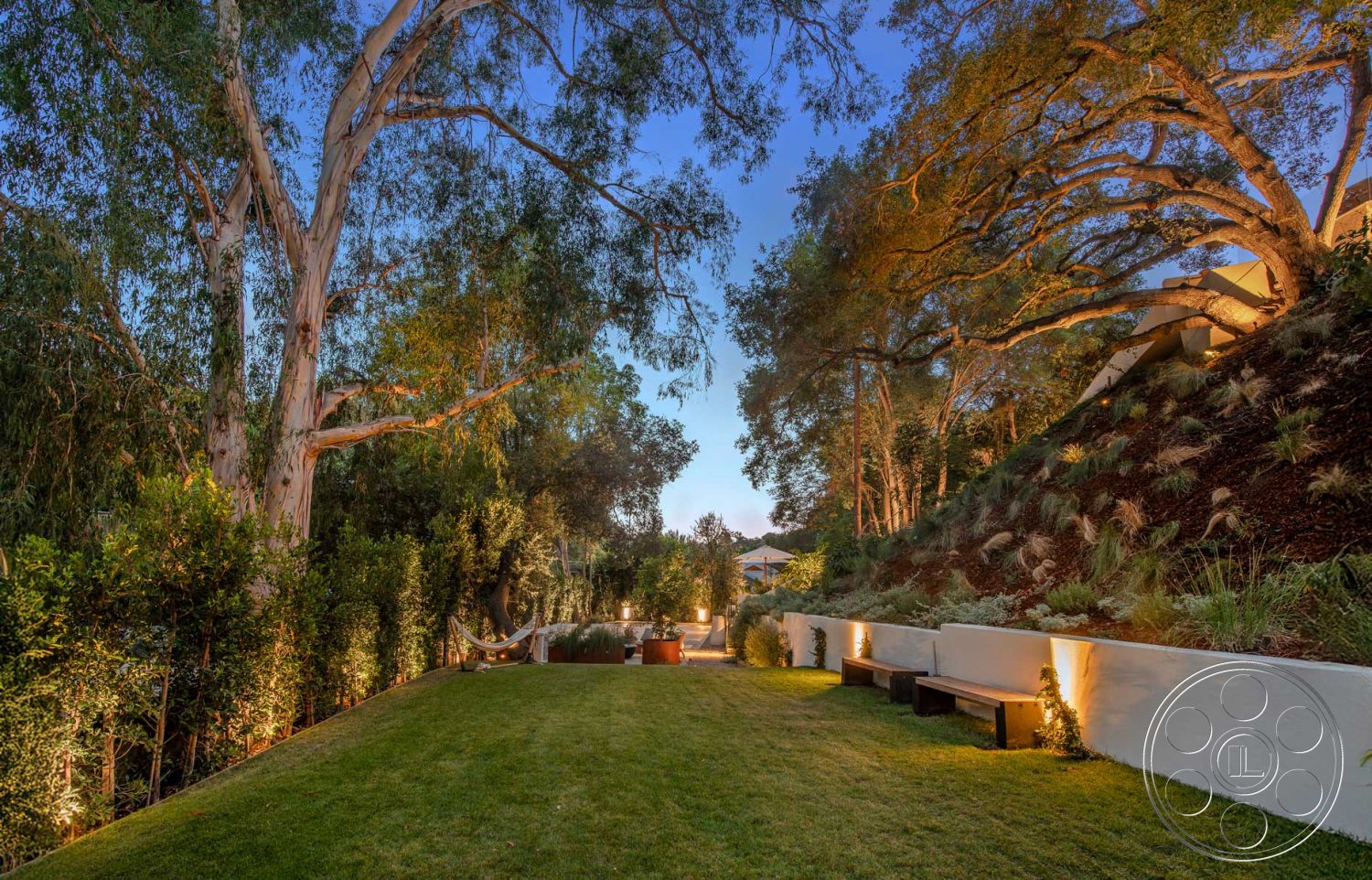 Modern 520 - exterior, landscaped backyard, wooden bench seating, lawn area, natural stone path, outdoor relaxation area, eucalyptus trees, hedge borders, native plant garden, ambient garden lighting, urban suburban blend, concrete garden wall, hammock setup, slope landscaping, evening outdoor ambiance