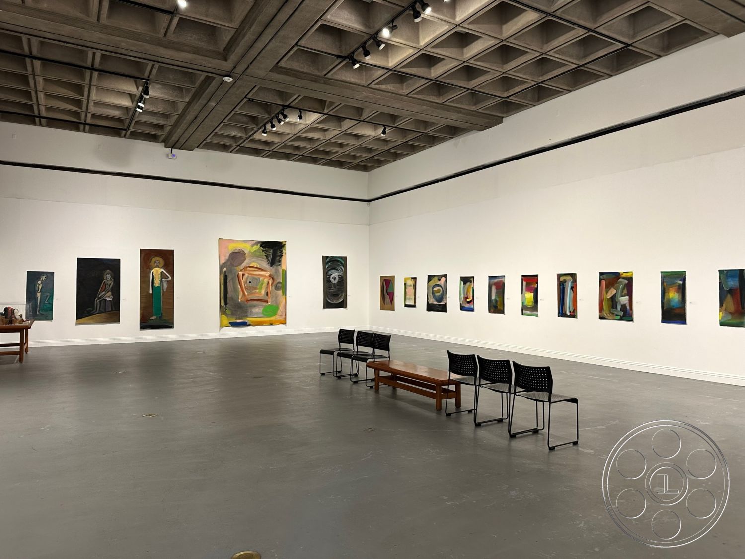 Art Gallery DTLA - neutral color palette, open floor plan, industrial style, exposed concrete ceiling, modern seating area, glass display cases, steel frame construction, track lighting fixtures, concrete gallery flooring, drywall gallery walls, rectangular art display layout, minimalist wooden bench, simple stacking chairs, art installation space, interior gallery setting, high ceiling with grid pattern, work of art arrangement, abstract art collection, contemporary art exhibits