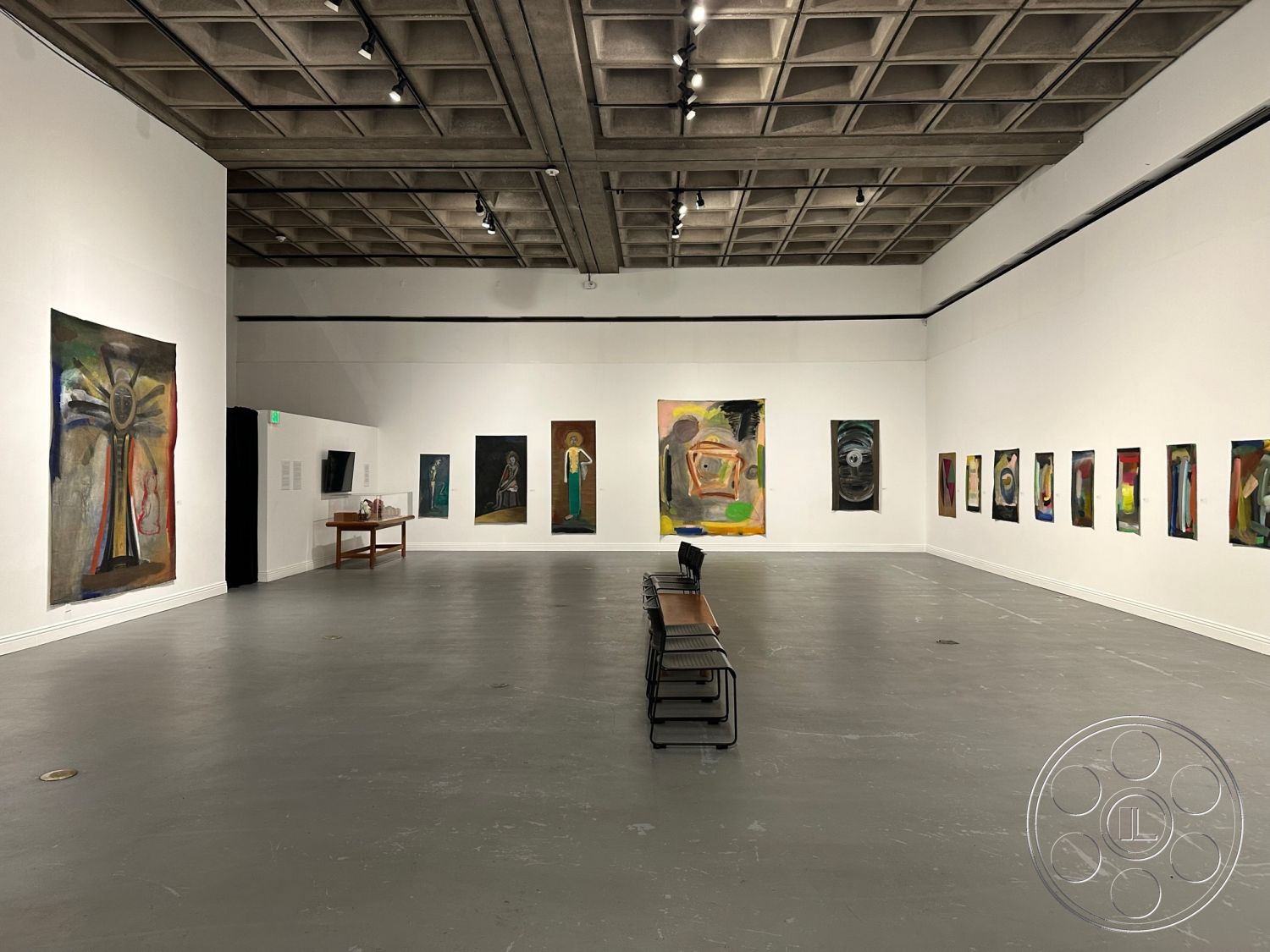 Art Gallery DTLA - high ceilings, neutral color palette, polished concrete floor, open floor plan, floor-to-ceiling windows, exposed concrete ceiling, clean lines and geometric forms, track lighting fixtures, minimalist interior, industrial style architecture, rectangular art display layout, white painted gallery walls, gallery space with modern artwork, modern wooden display table, dark wood bench seating, urban art gallery setting, exhibition space for contemporary art