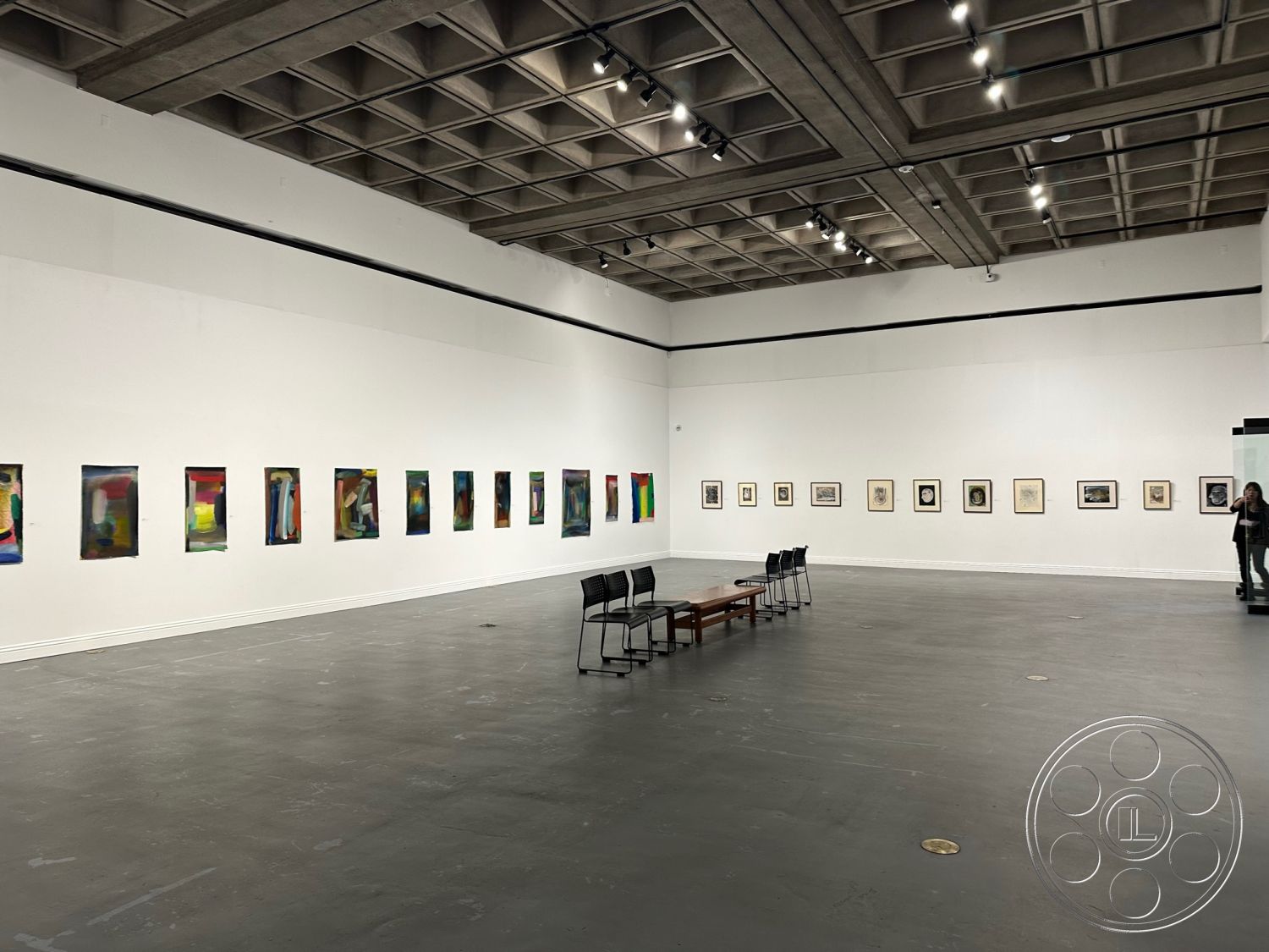 Art Gallery DTLA - neutral color palette, floor-to-ceiling window, open space concept, exposed concrete ceiling, cement flooring, minimalist design details, white painted walls, rectangular seating arrangement, track lighting fixtures, fluorescent ceiling lights, square room layout, polished concrete floor finish, modern art gallery interior, gallery wall with framed art, abstract paintings display, industrial style architectural features, contemporary gallery setting