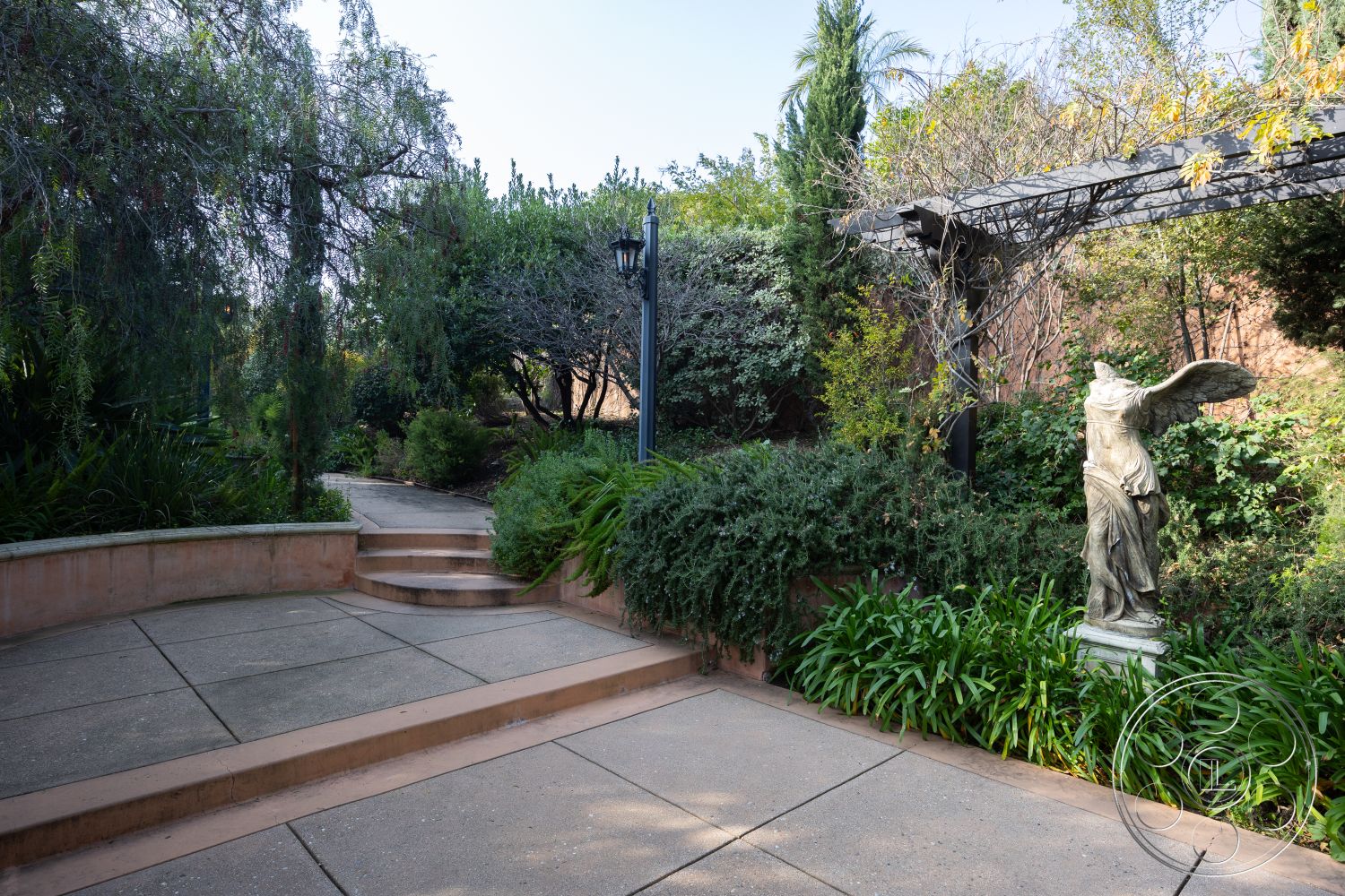 Mansion 145 - lush landscaping, suburban backyard, decorative outdoor lighting, tree-lined surroundings, concrete patio flooring, soft lighting ambiance, exterior patio area, city garden setting, curved stone steps, tiled garden pathway, ornamental statue feature, pergola structure, varied shrubbery and plants