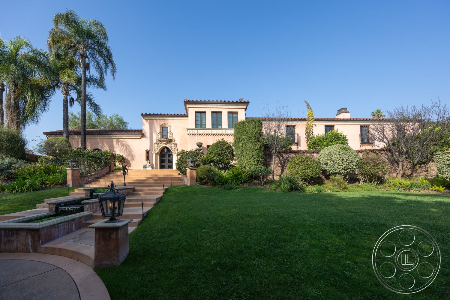 Mansion 145 - terracotta roof tiles, arched entryway, Mediterranean architectural style, stucco exterior walls, landscaped garden patio, sunny outdoor environment, neatly trimmed hedges, lush greenery surrounding property, decorative wrought iron details, palm trees in suburban setting, stone steps leading to entrance, circular driveway with manicured lawn, brick accent wall surrounding property, metal lanterns on pathway, modern double-hung windows, encrypted outdoor lighting, tile walkway, exposed wood beams on roof, private backyard with grass lawn, home with multiple elevations