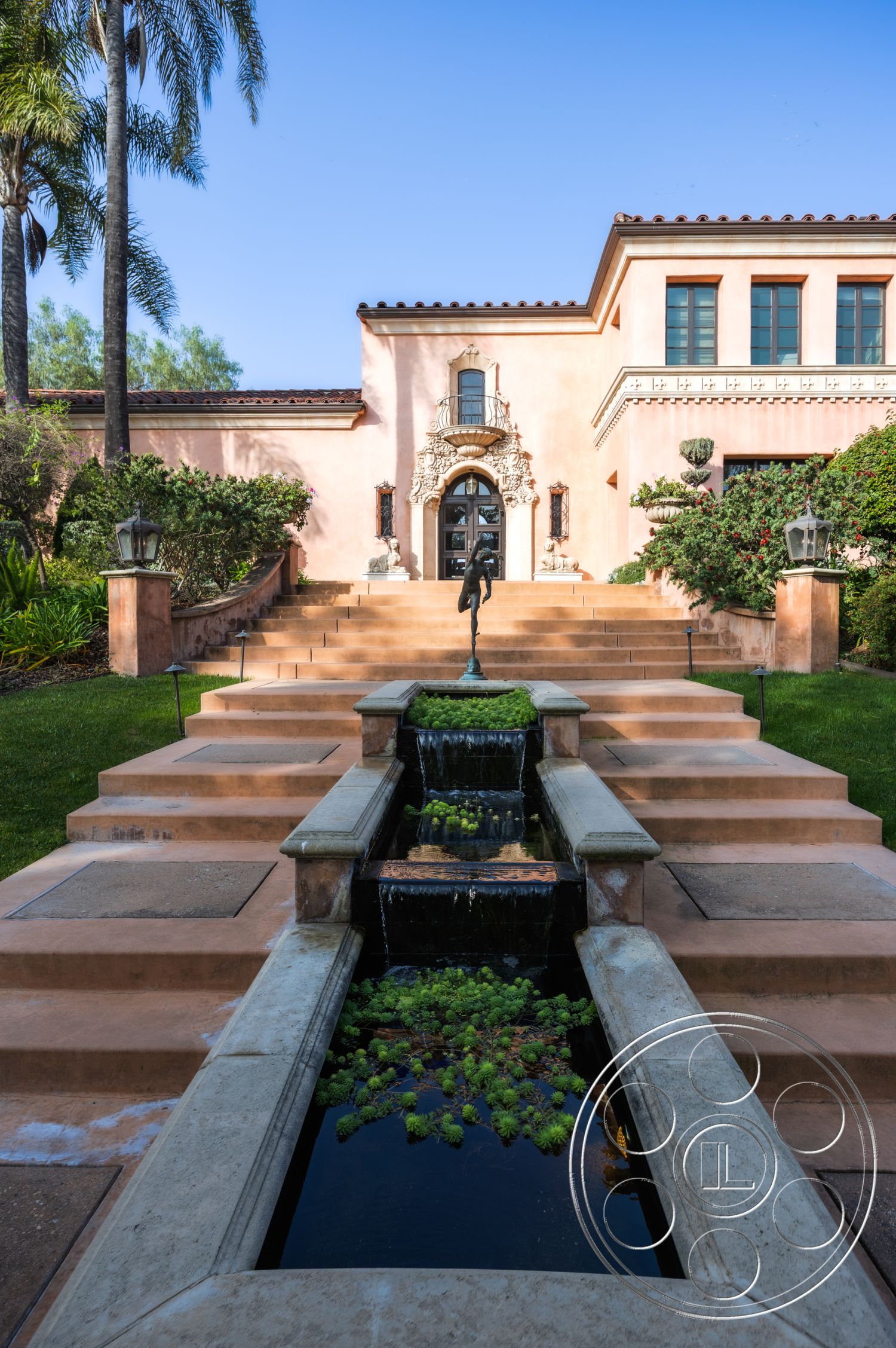 Mansion 145 - terracotta roof tiles, arched entryway, stone steps, lush greenery backdrop, decorative stone planters, modern outdoor lighting fixtures, symmetrical façade, rectangular water feature, exterior plaster walls, concrete landscaping steps, lush tropical garden setting, ornate door details, architectural molding accents, short retaining wall, framed garden view, fountain with lilies, two-story residential design