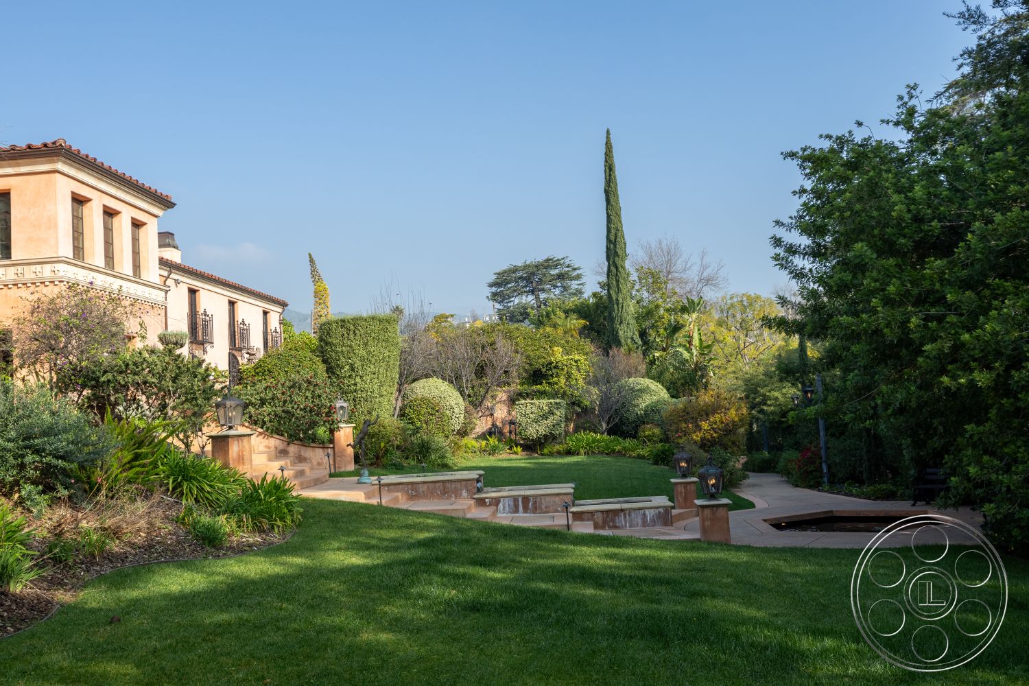 Mansion 145 - natural stone accents, outdoor seating area, red tile roof, arched doorways, Mediterranean architectural style, terraced lawn, landscaped garden setting, exterior stucco walls, concrete patio floor, low-maintenance shrubbery, symmetrical garden layout, casual outdoor living space, circular stone steps, planted trees for shade, decorative stone landscape features