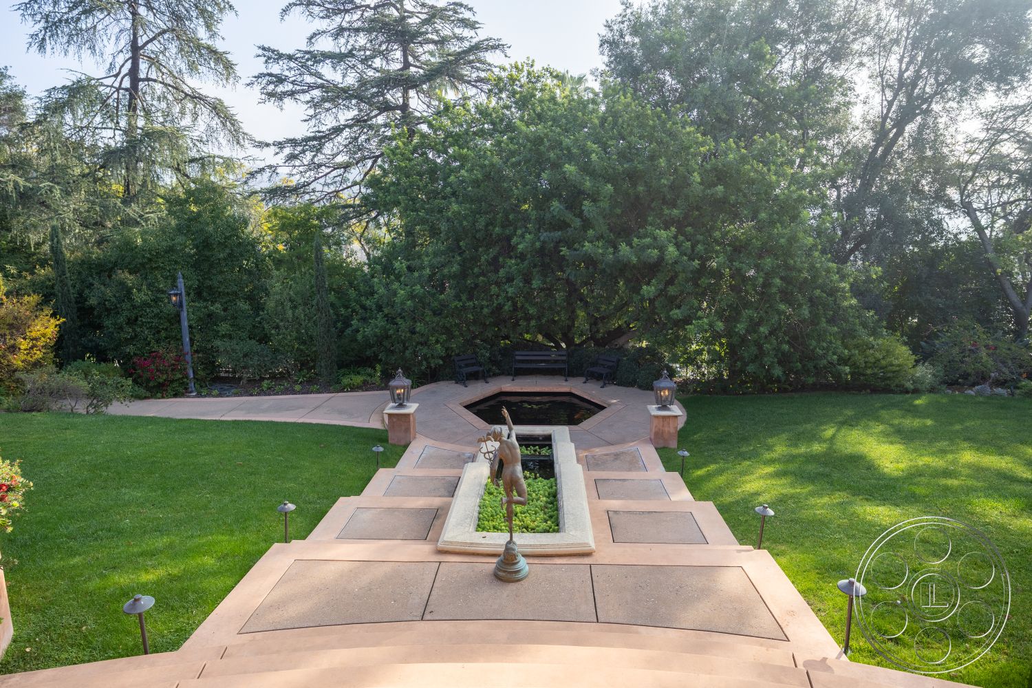 Mansion 145 - surrounding greenery, curved pathway, flowering shrubs, paved pathway, elevated view, decorative lanterns, lush garden, natural wood benches, multi-level landscaping, vegetation border, wooden seating area, exterior landscape setting, concrete patio steps, rectangular garden pond, square lawn area, lamp post lighting, stone water feature, open space lawn