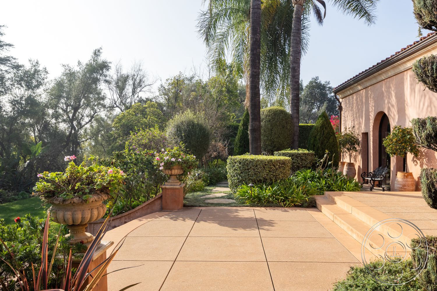 Mansion 145 - tropical palm trees, manicured hedges, natural stone steps, ornamental flower pots, landscaped garden setting, exterior concrete patio flooring, stamped concrete terrace surface, decorative outdoor seating area, arched doorways in warm stucco facade, lush greenery and flowering plants