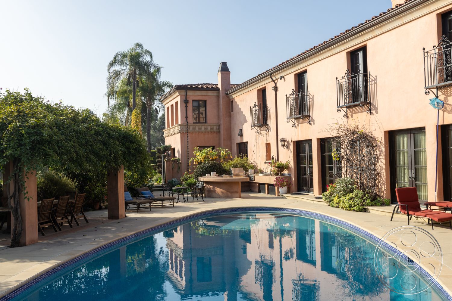 Mansion 145 - paved walkway, terracotta roof tiles, vintage outdoor furniture, arched windows, metal balcony railings, rounded swimming pool, tropical palm trees, Mediterranean architectural style, stone pool deck, lush greenery surroundings, exterior stucco walls, landscaped garden patio, sun-drenched pool area, wooden outdoor dining table, garden with flowering plants, tile patio flooring, open-air lounging area, decorative planters with flowers, modern glass door entrances, hacienda-inspired design