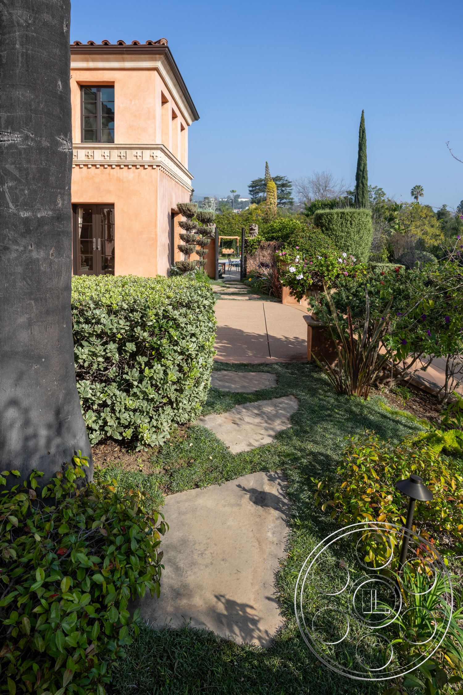 Mansion 145 - potted plants, landscaped yard, terracotta accents, ornamental shrubs, Mediterranean architectural style, flagstone pathway, exterior stucco wall, urban garden setting, lush greenery landscape, garden lighting fixtures, blue sky backdrop, decorative concrete patio, paved garden walkway, circular shaped flower bed, textured garden wall, designed outdoor seating area, traditional roof tiles