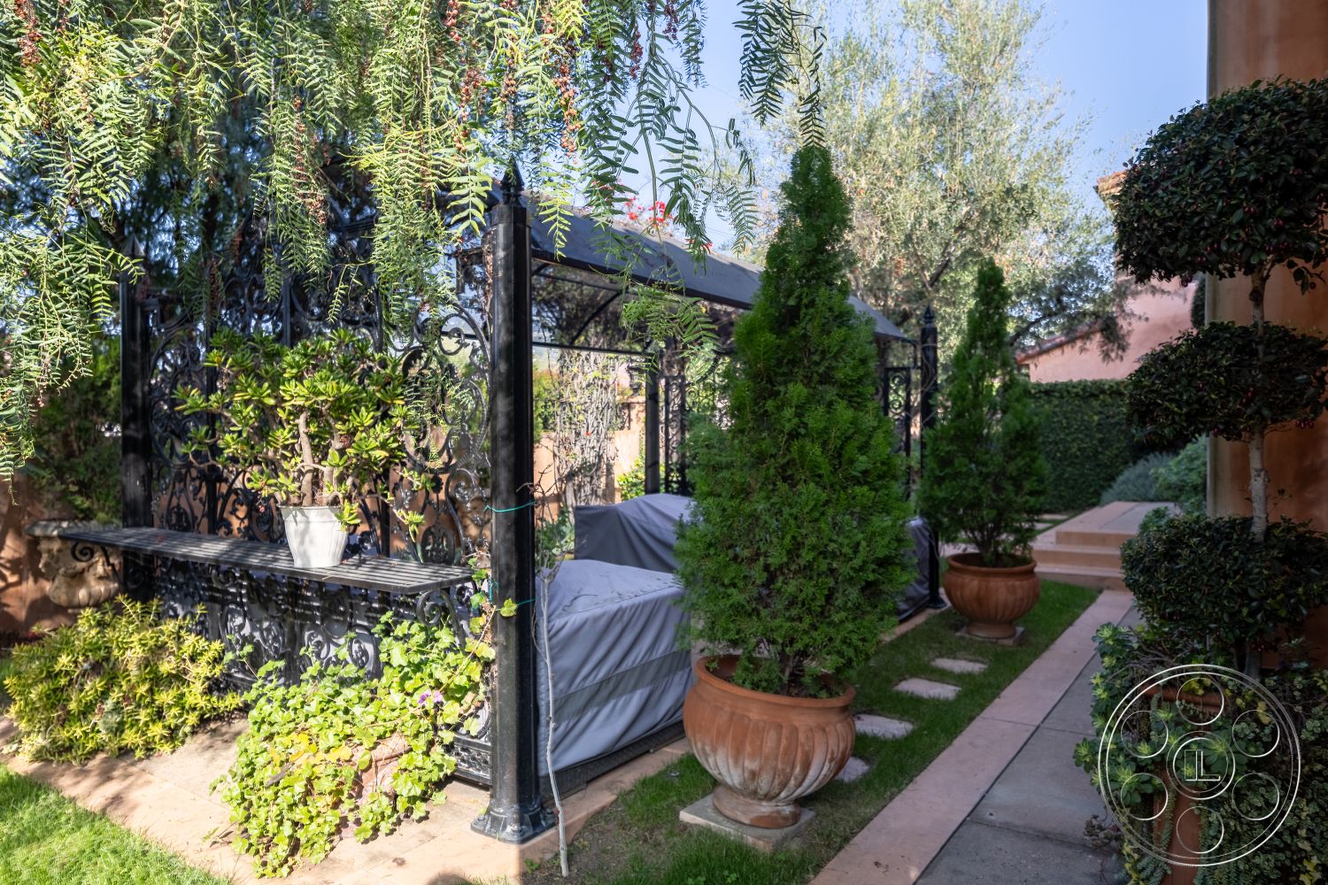 Mansion 145 - landscaped garden, sunny outdoor space, contemporary garden design, lush greenery surrounding, concrete patio area, exterior garden setting, curved stone pathway, potted succulent plants, wrought iron bench, decorative pebble border, topiary evergreens, pergola with decorative detailing, planter pots with drainage