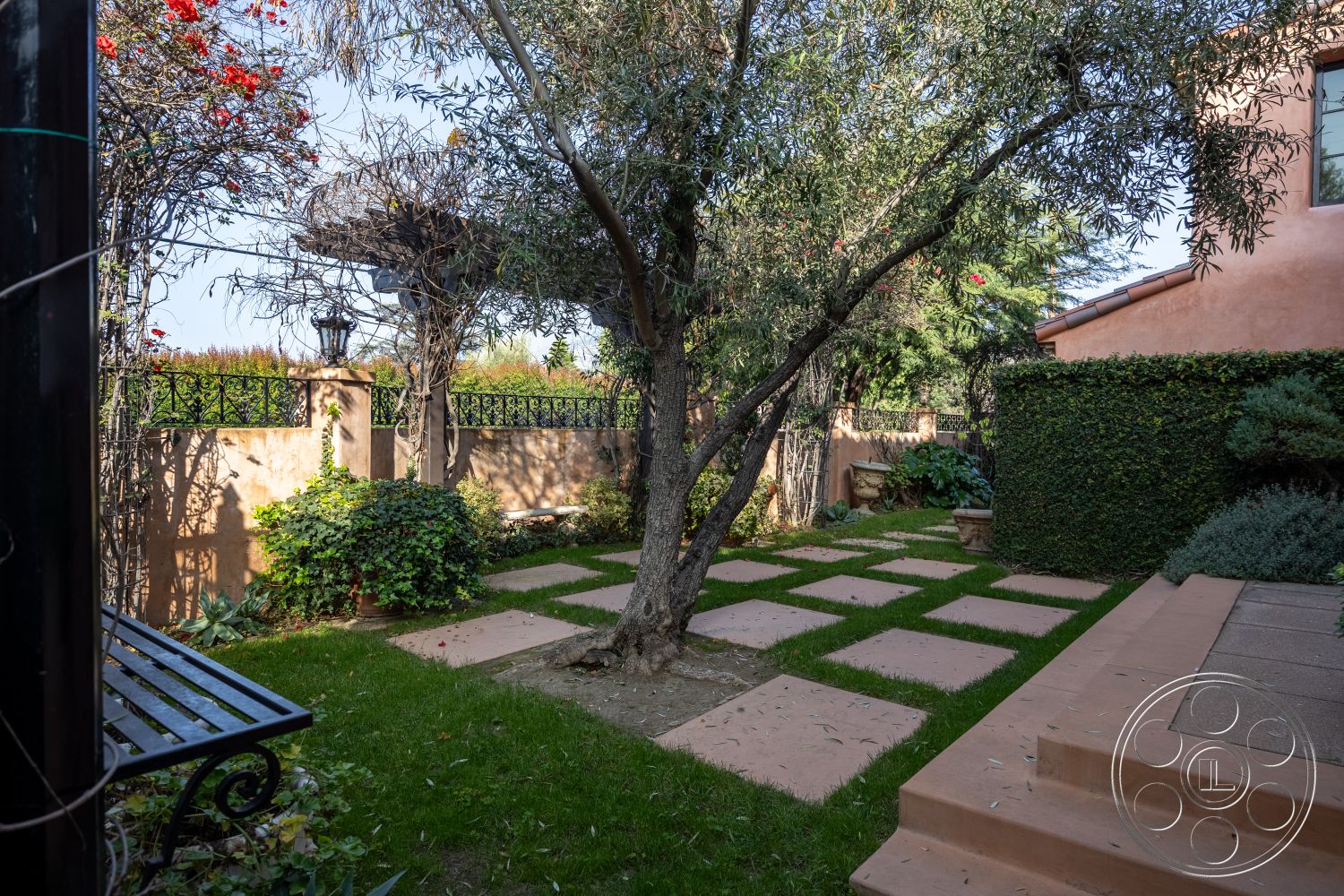 Mansion 145 - outdoor seating area, curved pathways, terracotta planters, concrete stepping stones, natural grass lawn, exterior garden setting, green shrubbery accents, olive tree landscaping, pergola structure, stucco garden walls, decorative iron fence, paved patio steps, seasonal floral accents