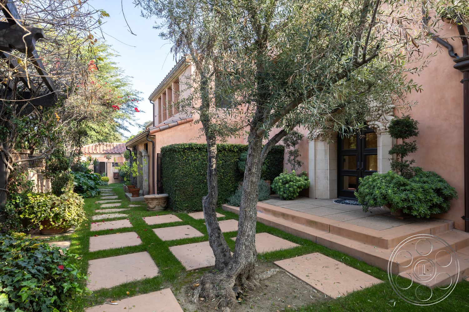 Mansion 145 - exterior, landscaped garden, terracotta tile roof, ornamental shrubs, Mediterranean architectural style, green lawn area, arched entry door, low-maintenance greenery, plaster exterior walls, stone steps entryway, concrete pathway pavers, olive trees in garden, flagstone stepping stones, decorative door architrave, cast stone accent details, tiled patio steps, lush foliage surroundings, garden pots with plants