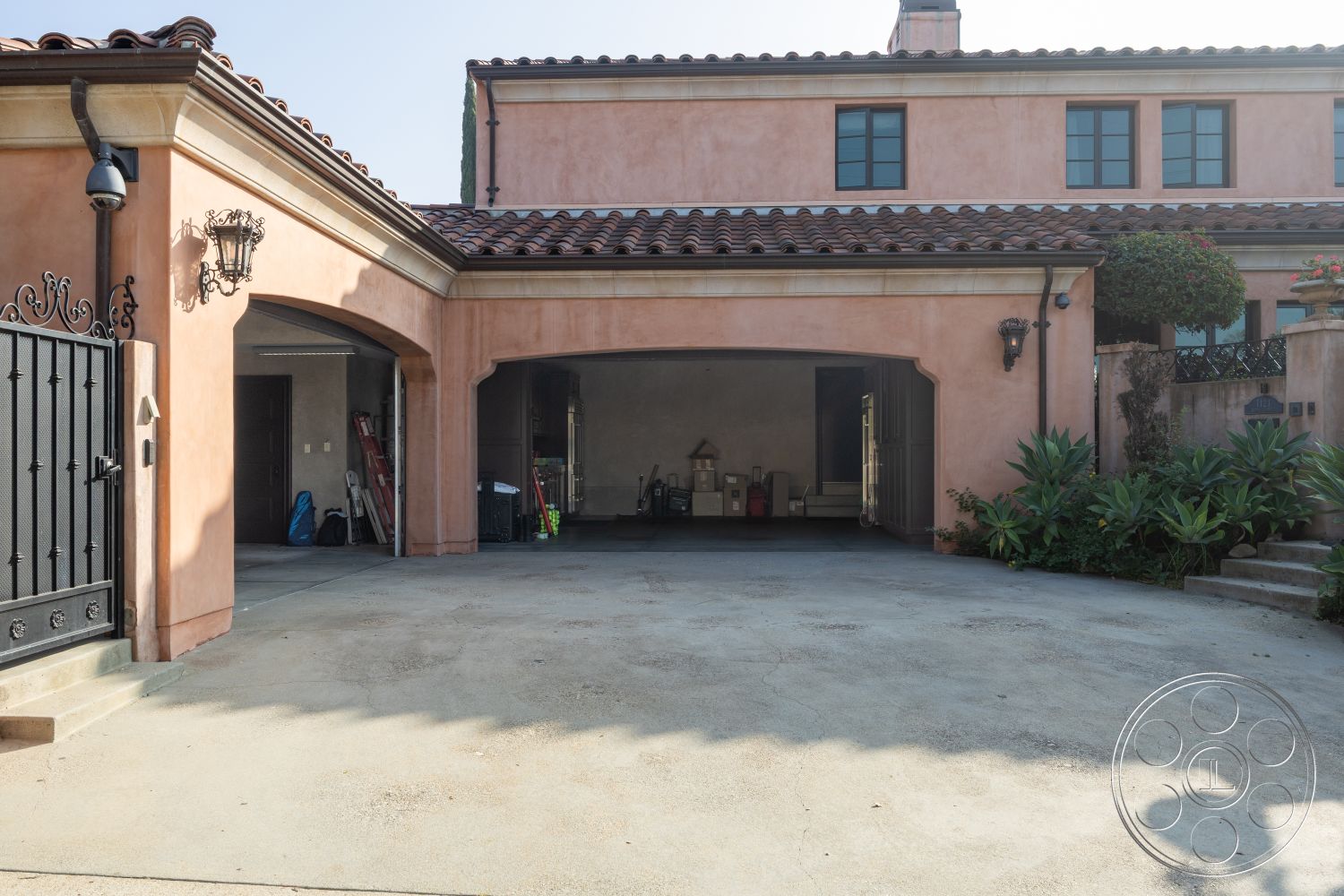 Mansion 145 - black wrought iron gate, stucco exterior walls, textured stucco finish, landscaped garden beds, stamped concrete driveway, exterior wall lanterns, terra cotta tile roof, exterior driveway, potted plants decoration, dark wood garage doors, arched garage entrance, curvy pathway