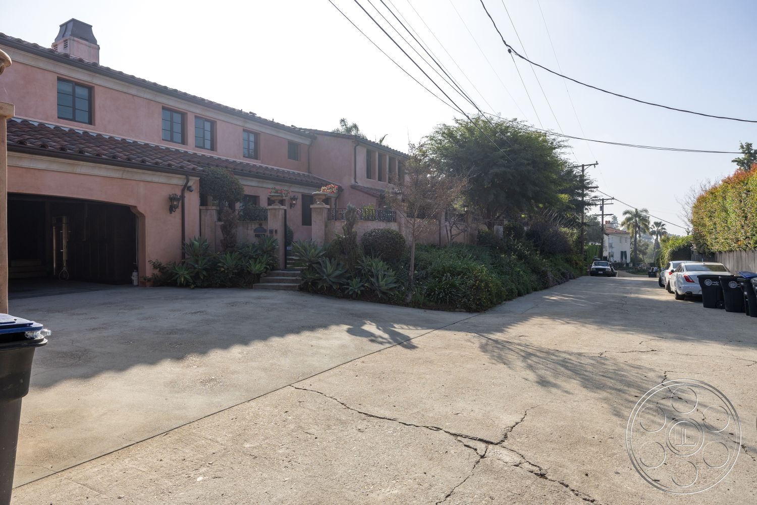 Mansion 145 - exterior, concrete driveway, red tile roof, arched entryway, wooden garage door, decorative wall sconces, outdoor steps, two-story home, stucco house exterior, landscaped garden beds, native plants landscaping, modern residential setting, city alley view, urban suburban mix