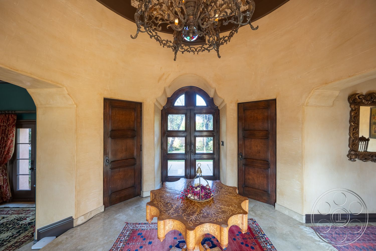 Mansion 145 - vaulted ceiling, chandelier lighting, arched doorways, textured plaster walls, dark wood paneling, spacious foyer, window with grid pattern, decorative wall mirror, natural light entry, intricate crown molding, solid wood doors, round decorative table, persian area rug, rustic wooden accents