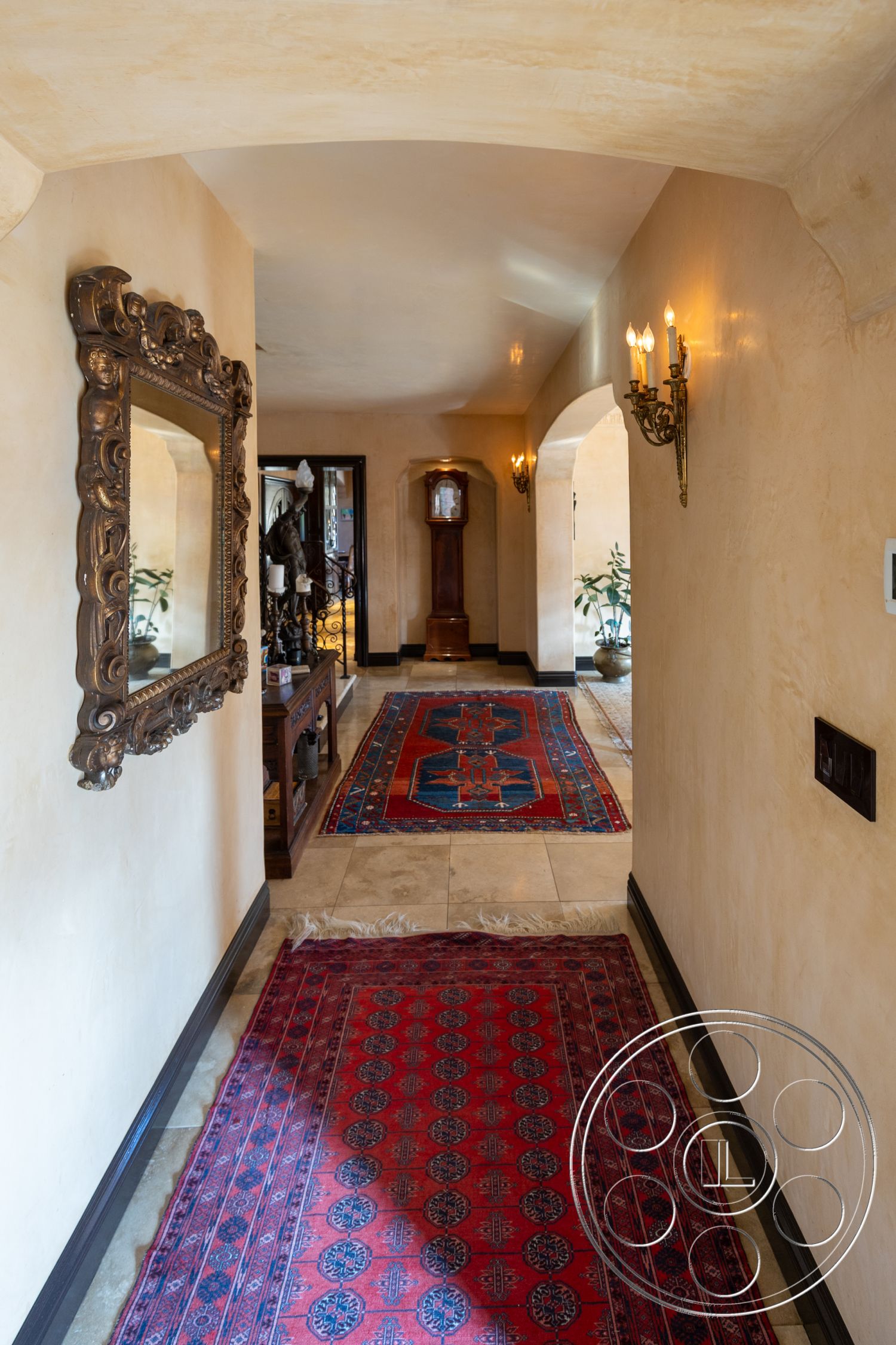 Mansion 145 - arched doorways interior, plastered wall treatment interior, decorative mirror frame interior, classic wall sconces interior, wooden baseboard trim interior, stone tile flooring interior, oriental rug accent flooring, antique grandfather clock feature interior, living room corridor space interior, interior decorative wall lighting, narrow hallway design interior, traditional style interior decor, textured plaster wall finish interior