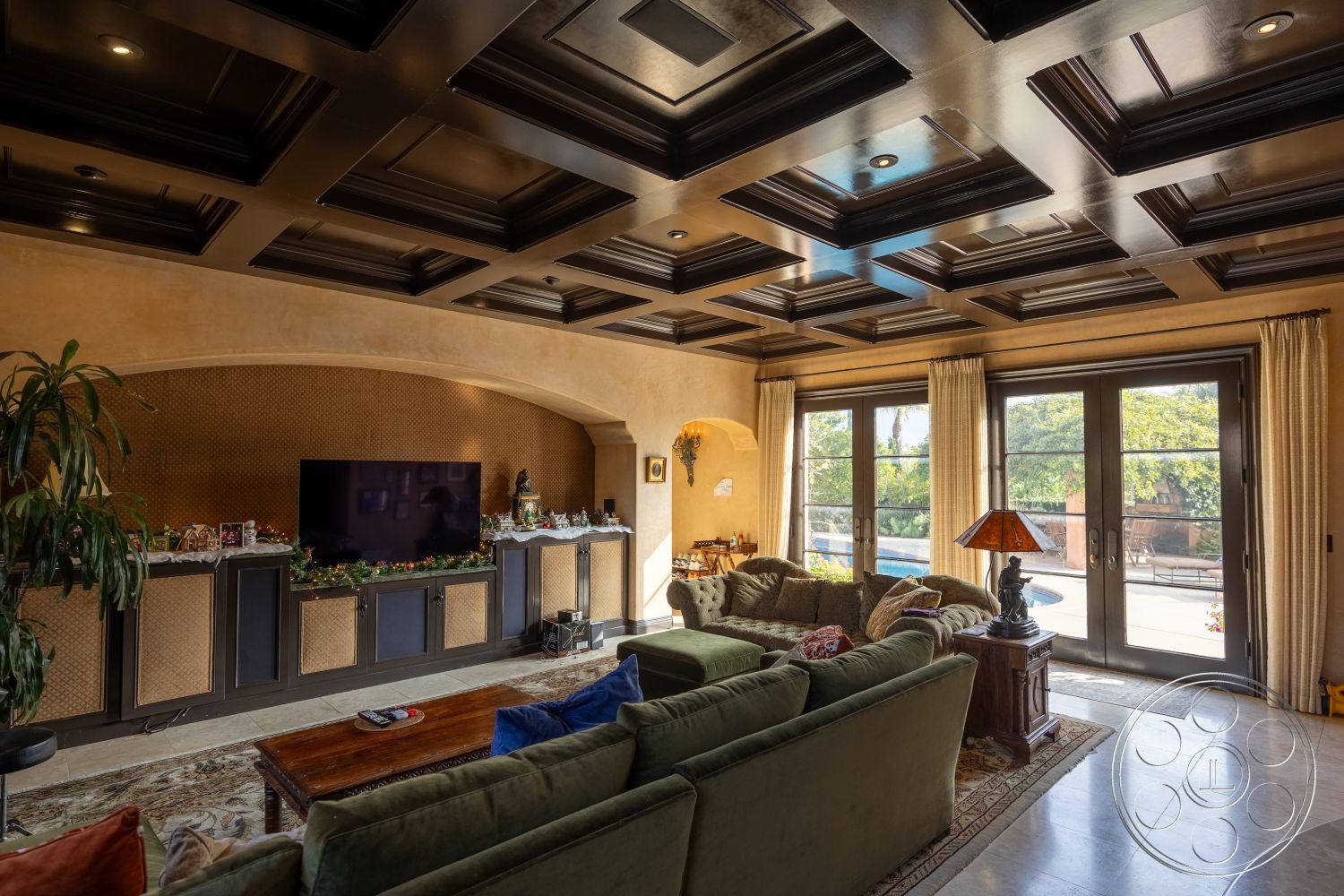 Mansion 145 - large glass doors, soft beige wall color, textured plaster walls, natural light from windows, dark wood ceiling beams, interior living space, modern sectional sofa, wall-mounted TV unit, spacious open layout, indoor plant accents, coffered ceiling design, understated decor elements, decorative console table, tile flooring in living room, elegant window drapery, suburban home aesthetic, pool view from living area, traditional artwork display