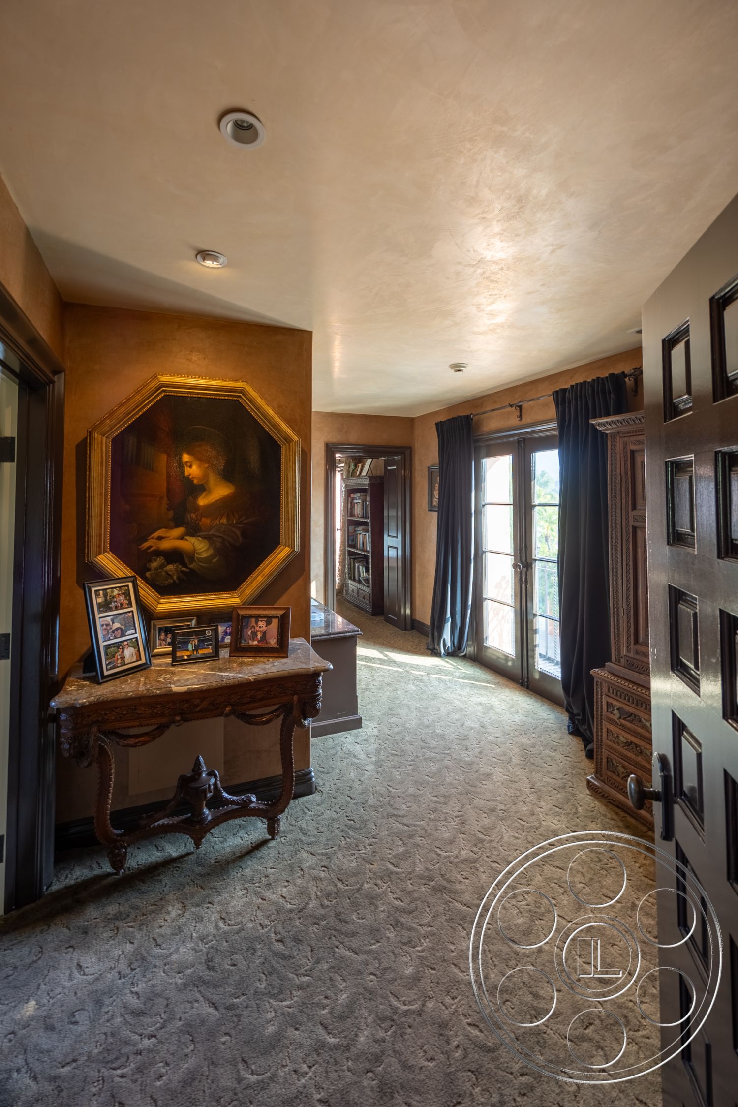 Mansion 145 - cozy atmosphere, floor-to-ceiling windows, beige wall color, textured plaster walls, ornate ceiling details, decorative moldings, spacious entryway, transitional decor, interior hallway, soft carpet flooring, natural light from exterior, traditional interior style, traditional hardwood console table, framed family photographs, octagonal framed artwork, dark wood paneled doors, dark fabric drapes, classic art piece