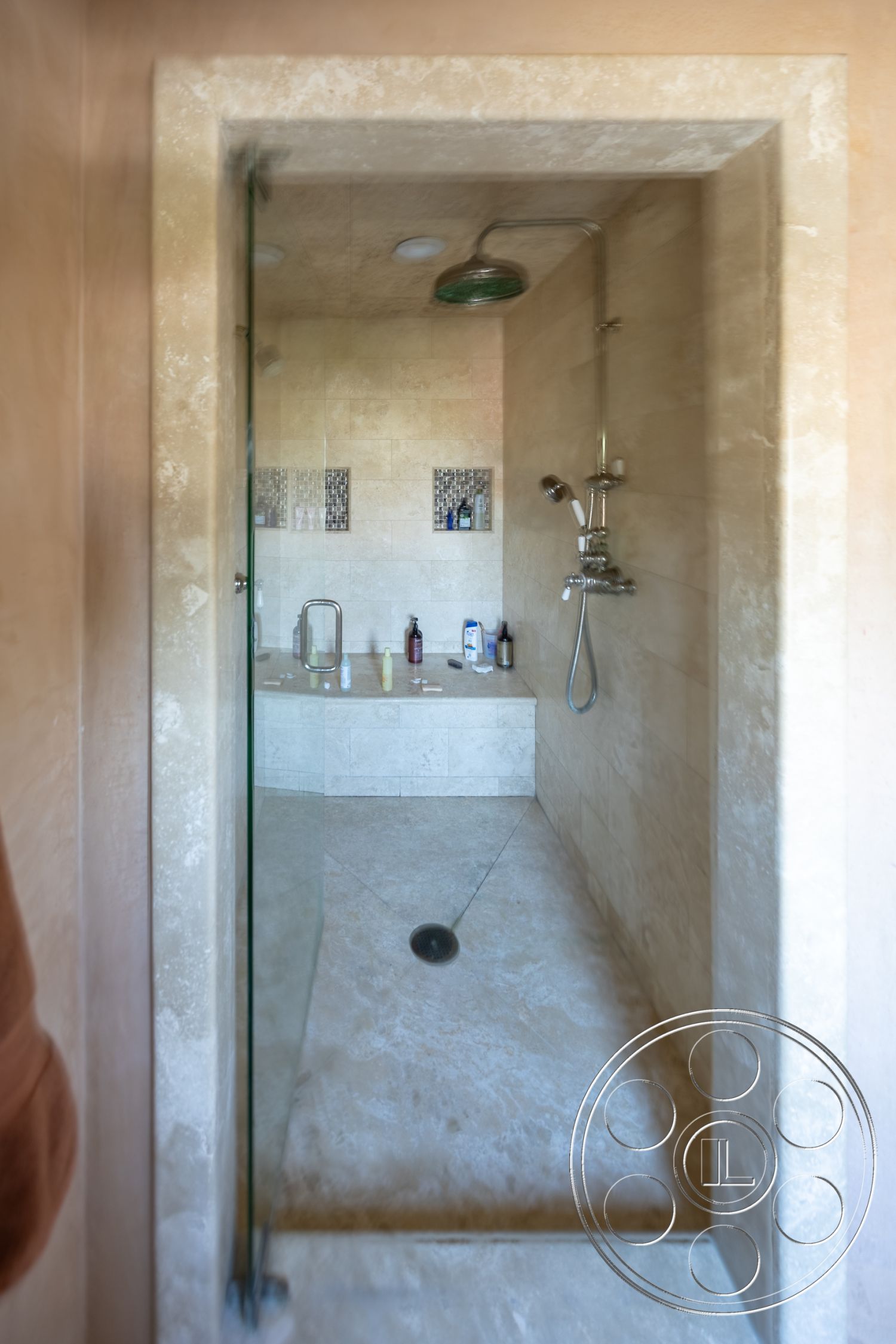 Mansion 145 - glass shower doors, interior shower space, seamless glass enclosure, rectangular shower layout, minimalist shower design, travertine stone shower walls, smooth travertine shower floor, built-in shower shelves, wall-mounted shower fixture, overhead rain showerhead, linear drain design, neutral beige color palette, textured pebble wall accent, modern spa-like atmosphere