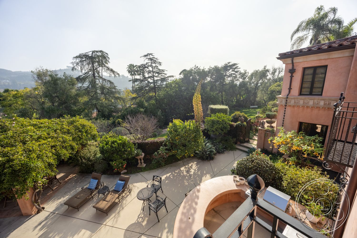 Mansion 145 - metal outdoor furniture, iron balcony railing, wooden lounge chairs, natural stone planters, exterior concrete patio floor, lush garden setting, curved patio design, mediterranean architectural style, urban hillside view, plaster exterior walls, tile outdoor barbecue area, mixed shrub landscaping, outdoor sun lounging area, arched doorways to garden, paved garden pathways