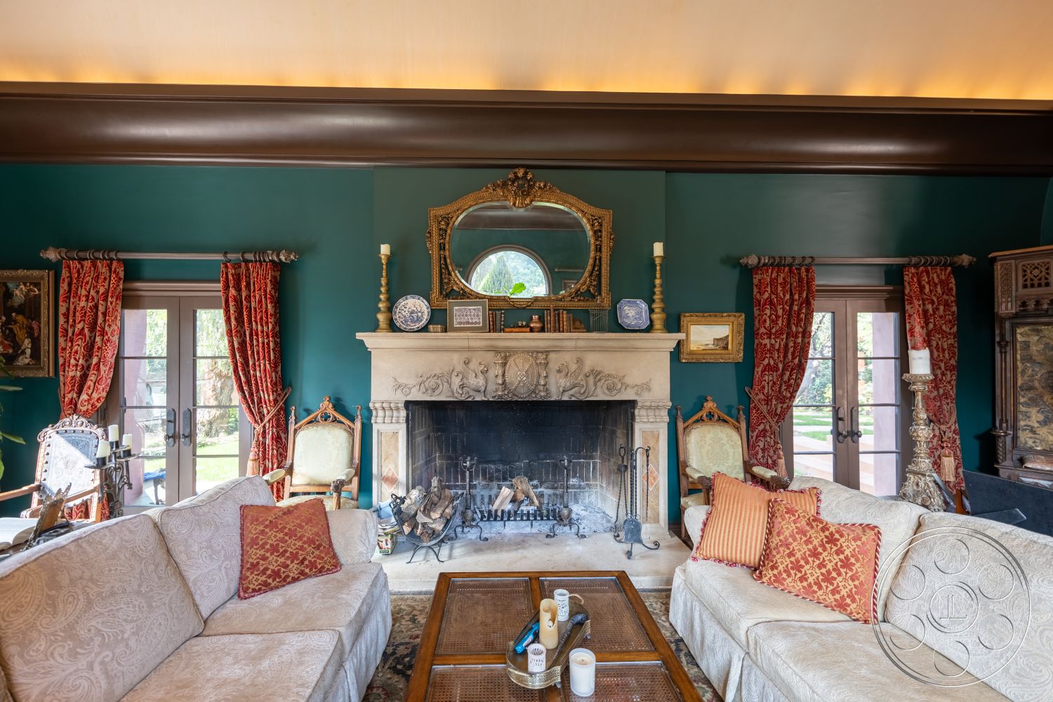 Mansion 145 - decorative wall art, plush throw pillows, plush fabric sofa, oval coffee table, interior living room, stone fireplace surround, wooden double doors, natural light from outdoor view, historic architectural style, vintage upholstered armchair, wood beam ceiling detail, ornate vintage mirror, red patterned drapes, neutral tone area rug, antique gold candlesticks, intricate wall moldings, baroque inspired decor