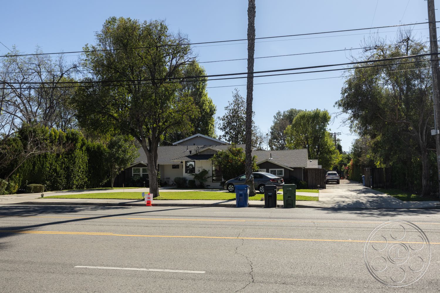 Clay Court - exterior, flat roof, palm trees, natural wood accents, curved driveway, asphalt driveway, fenced yard, wooden siding, open front porch, concrete driveway surface, ranch-style home, modern residential design, suburban neighborhood setting, landscape shrubs, front lawn with grass, large deciduous trees, driveway bordered by greenery, single-story bungalow, street view with power lines