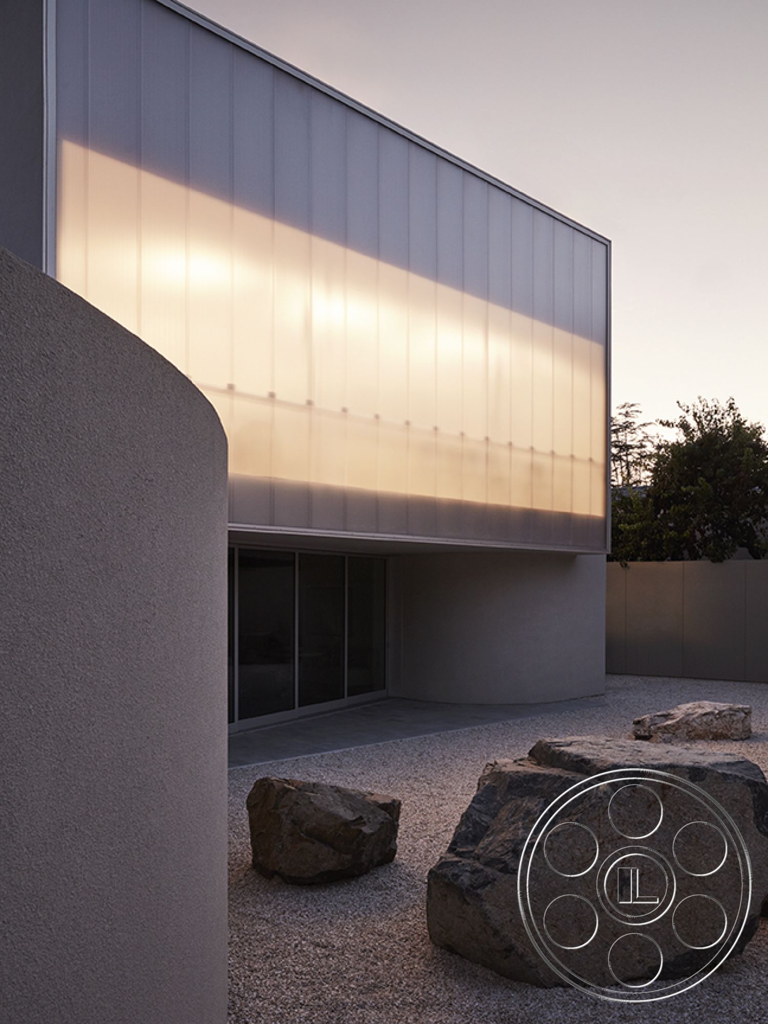 Modern 521 - seamless indoor-outdoor transition, contemporary outdoor space, modern minimalist design, floor-to-ceiling glass windows, curved architectural forms, polished concrete surface, open courtyard setting, natural stone feature elements, metal panel exterior wall, textured stucco exterior finish, gravel landscaping with boulders, soft natural lighting at dusk, landscaped garden environment, urban residential architecture, asymmetrical façade design