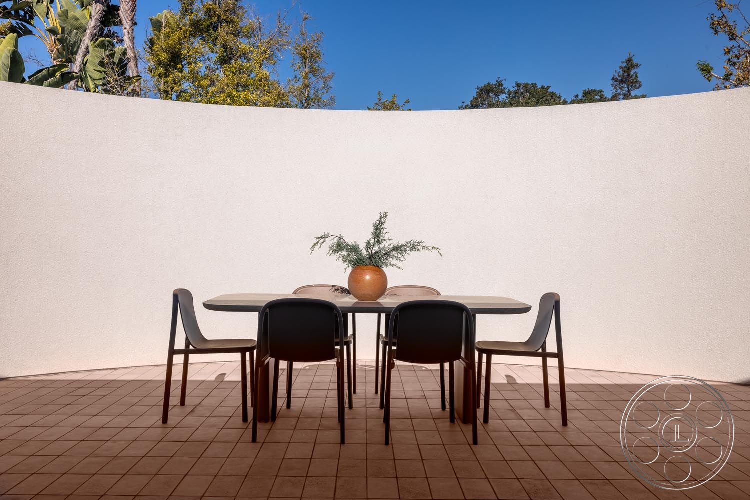 Modern 521 - textured plaster walls, curved wall design, terracotta tile flooring, sunny outdoor setting, modern round dining table, natural light exposure, contemporary design aesthetics, functional outdoor living space, interior exterior patio dining area, minimalist dining chairs, potted plant centerpiece, landscaped backdrop