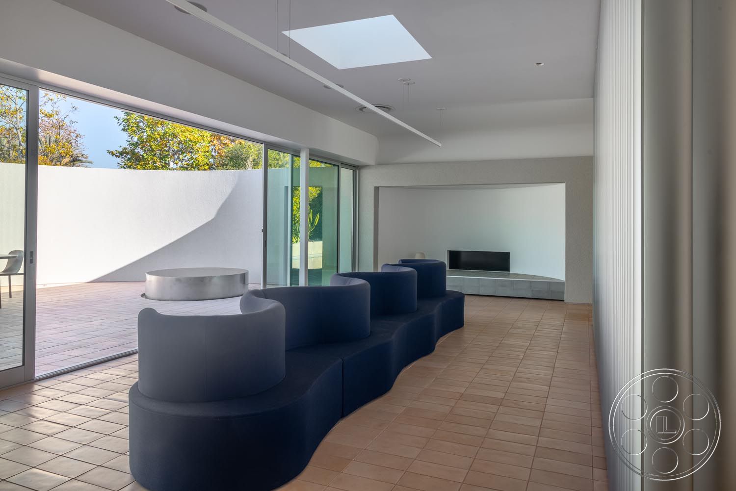 Modern 521 - urban setting, open-concept living space, large sliding glass doors, outdoor patio view, contemporary furniture design, natural light from skylights, geometric architectural details, plastered wall finish, white-painted walls, minimalist wall treatments, interior ceramic tile flooring, curved modern sofa seating, built-in television unit, smooth concrete accent walls, textured surface materials