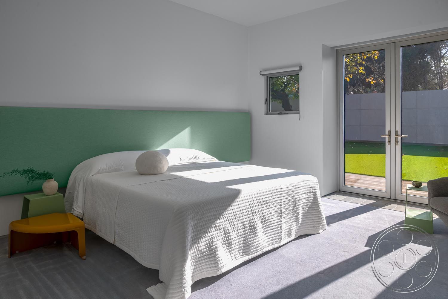 Modern 521 - minimalist aesthetic, open floor plan, neutral wall color, glass patio doors, low-profile furniture, minimalist bedside table, indoor plants as decor, interior bedroom with carpet flooring, flat panel green upholstered headboard, white quilted bedspread, modern decorative round pillow, yellow side table, natural light streaming through windows, contemporary window design, modern chair with sleek lines, green backyard view from bedroom, sliding door access to outdoor space