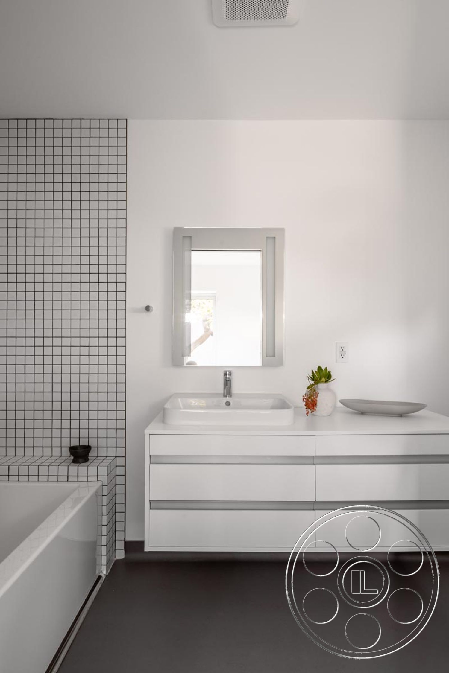 Modern 521 - interior bathroom with white painted walls, grid pattern ceramic tile feature wall, modern white cabinetry with flat panel drawers, rectangular undermount sink with single faucet, dark vinyl flooring in bathroom, minimalist mirror with sleek frame, contemporary countertop with clean lines, built-in seating area with tiled edge bathtub, lush green plant decor accent