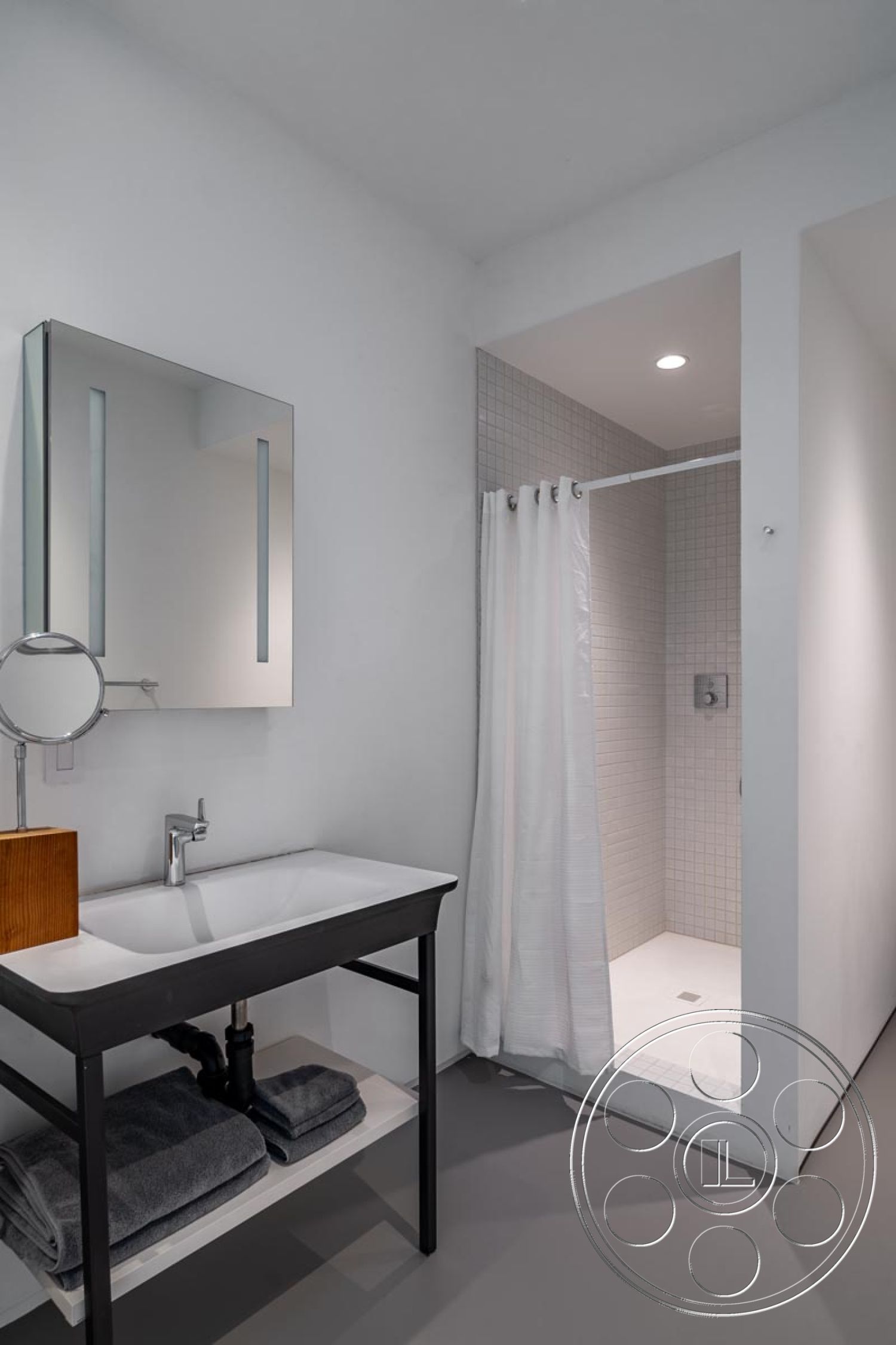 Modern 521 - minimalist design, monochromatic color scheme, recessed ceiling lighting, white painted walls, tiled shower floor, open shelving for towels, industrial style fixtures, linear shower drain, exposed tile shower walls, ensuite bathroom, black metal sink base, modern rectangular sink, mirror with vertical LED lighting, curtain enclosed shower area, gray rubber bathroom flooring, frameless glass shower partition