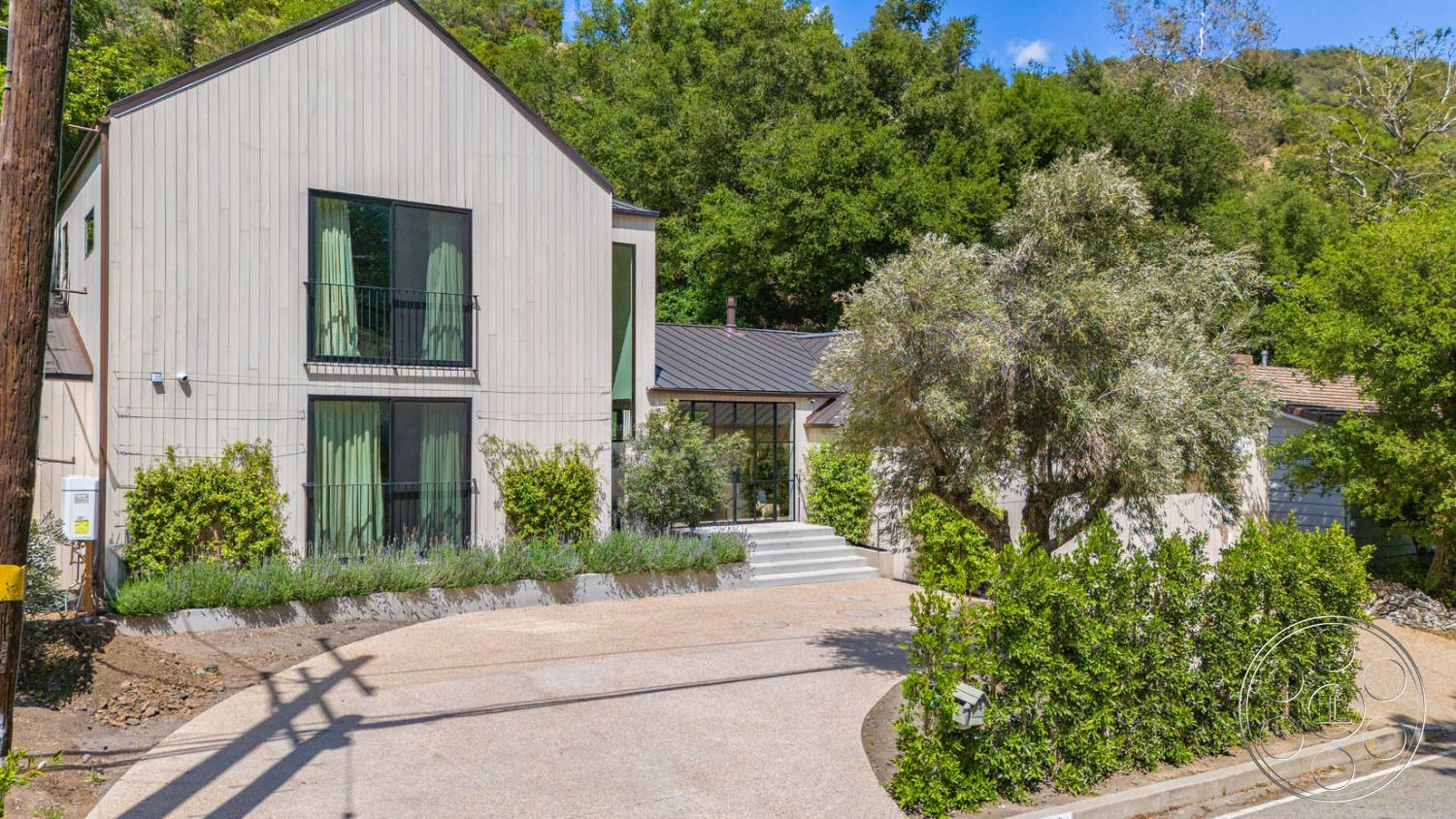 Modern Farmhouse 19 - glass sliding doors, outdoor seating area, suburban setting, floor-to-ceiling windows, concrete steps, curved driveway, mountain backdrop, metal roof, landscaped garden beds, natural stone border, open-concept entryway, exterior wood siding, two-story contemporary home, vegetation surrounding property, green curtain drapes, modern balcony railing